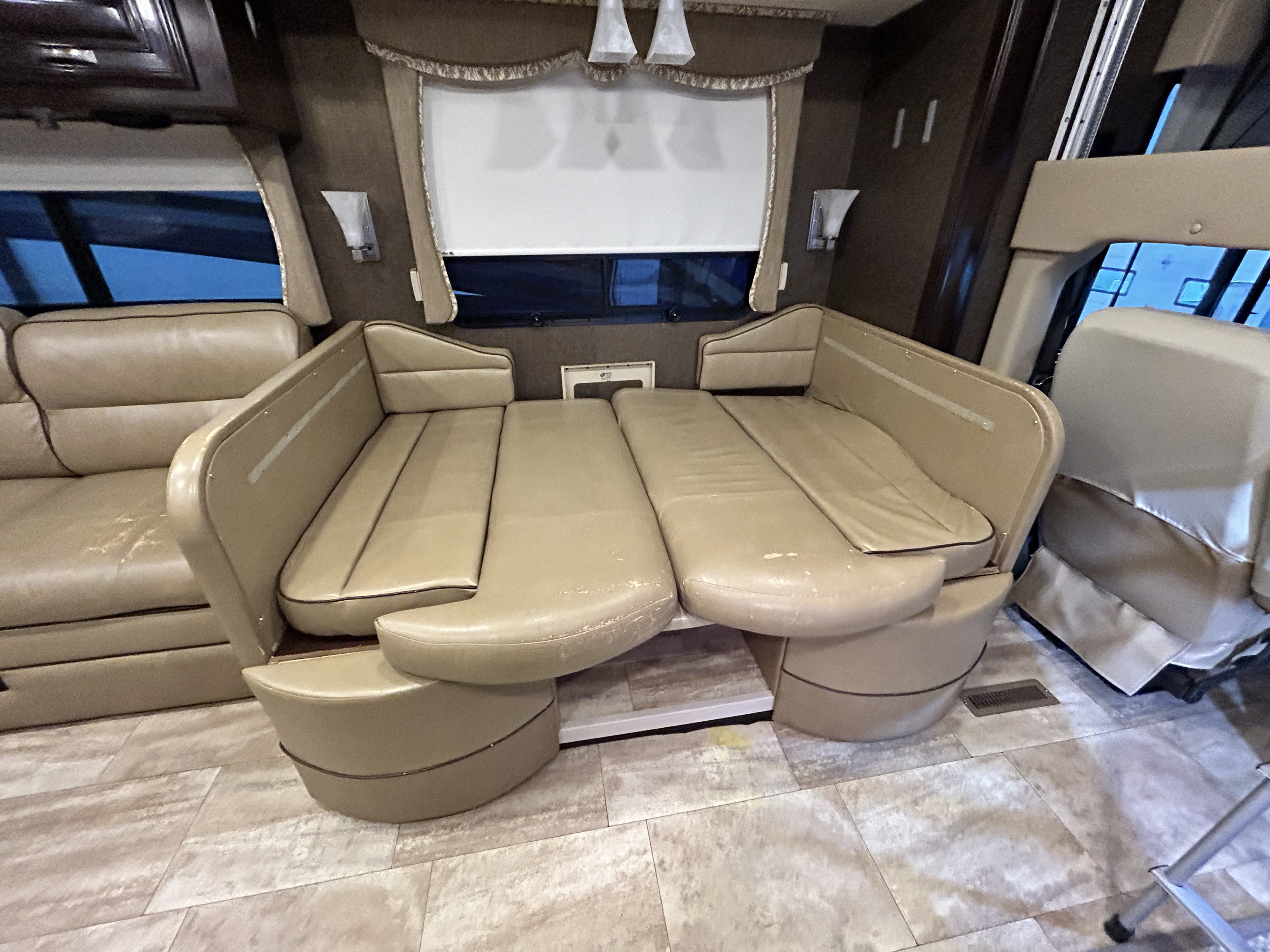 Inside an RV rental: Beige dinette seating converts to a bed, next to a large window with blinds, and light flooring.. Thor Motor Coach Challenger 2016