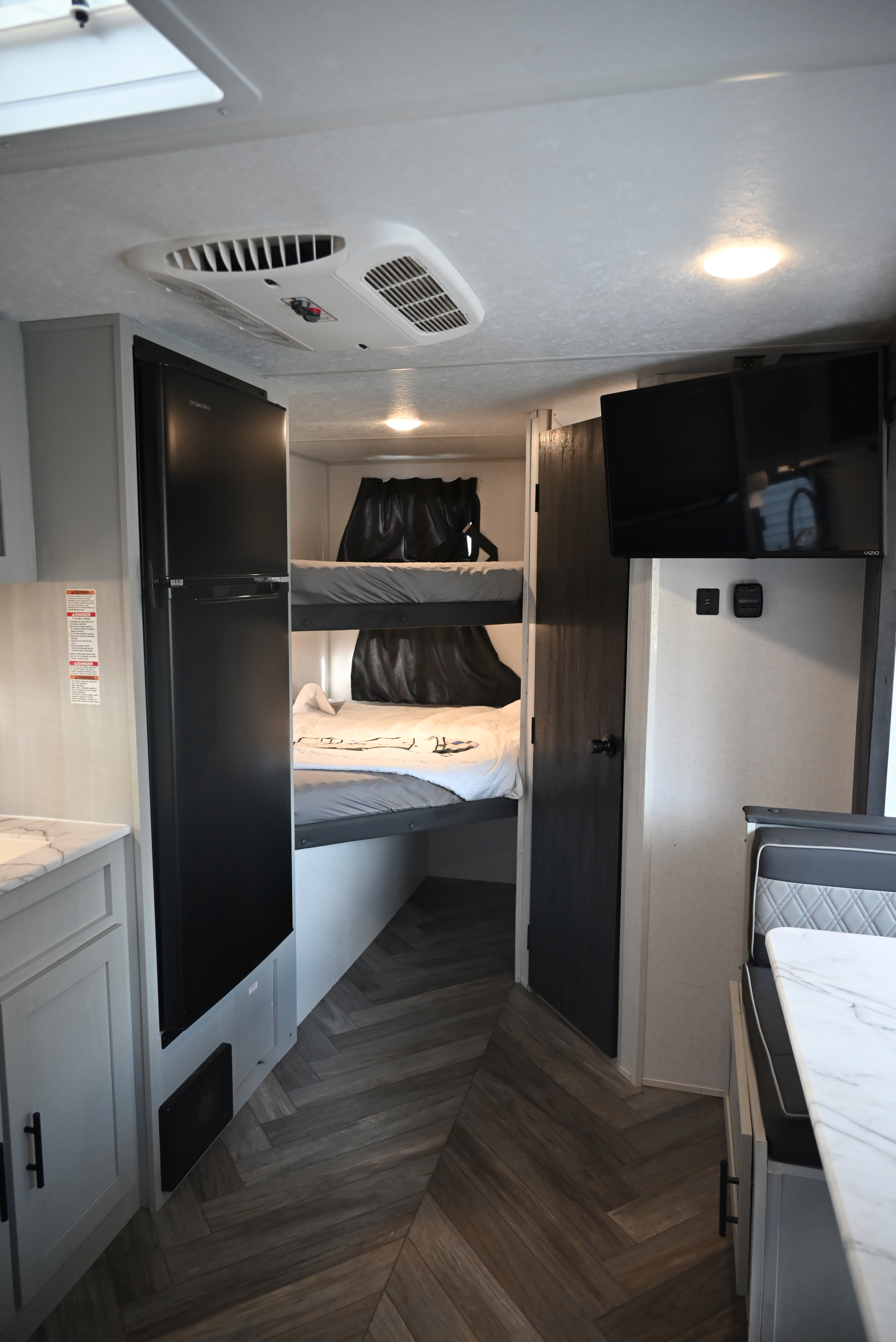 Modern RV rental interior with bunk beds, a black refrigerator, TV, and dinette area with a marble table.. Forest River Salem FSX 2022