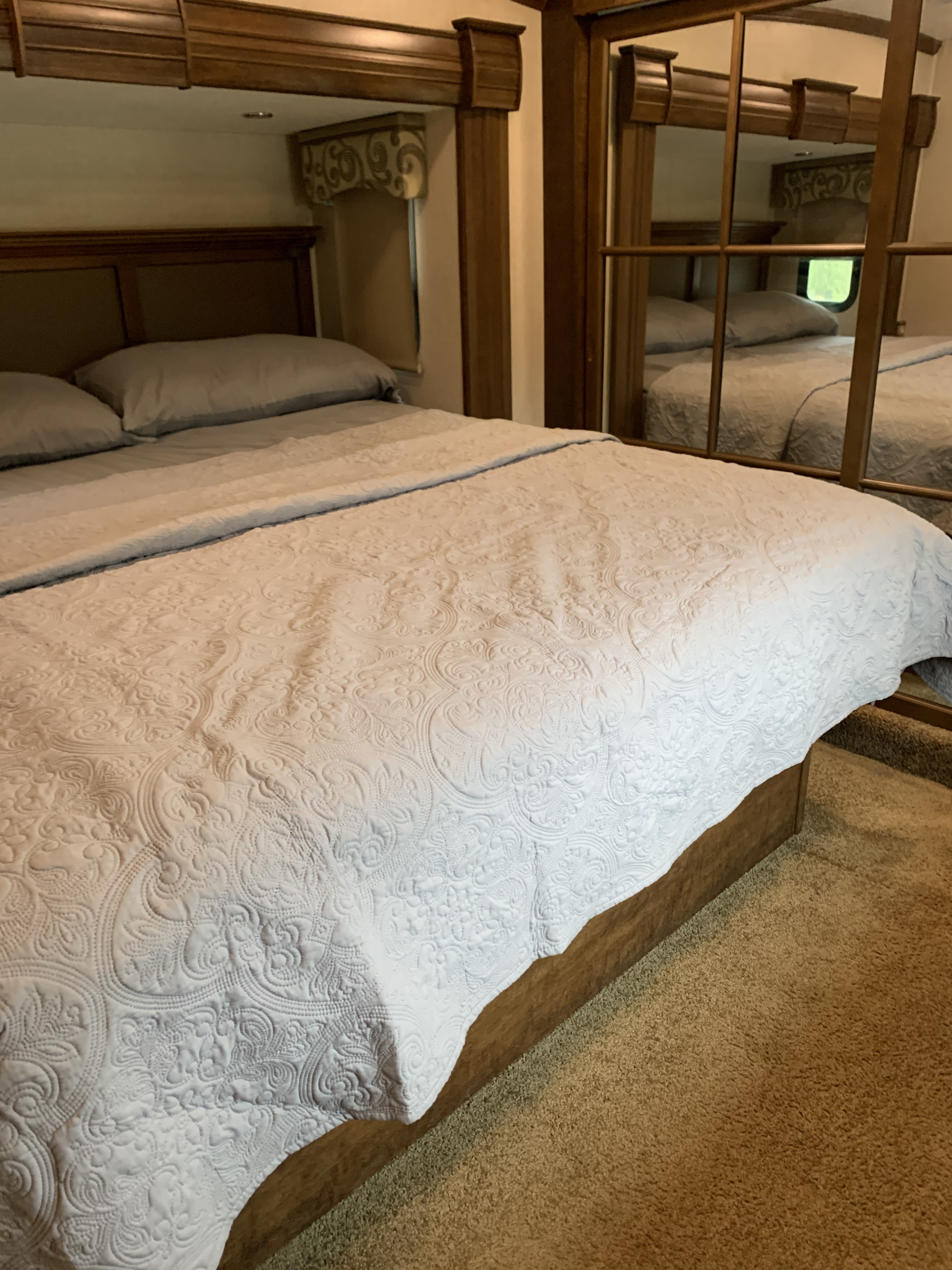 Experience comfort in this RV rental bedroom with a detailed quilted bedspread, cozy bed, & mirrored wardrobe.. Forest River Cardinal 2015