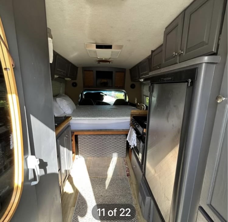 RV rental interior: Looking down the aisle to a bed. Kitchen appliances (fridge, stove) and gray cabinets line the space.. Ford Econoline 2004