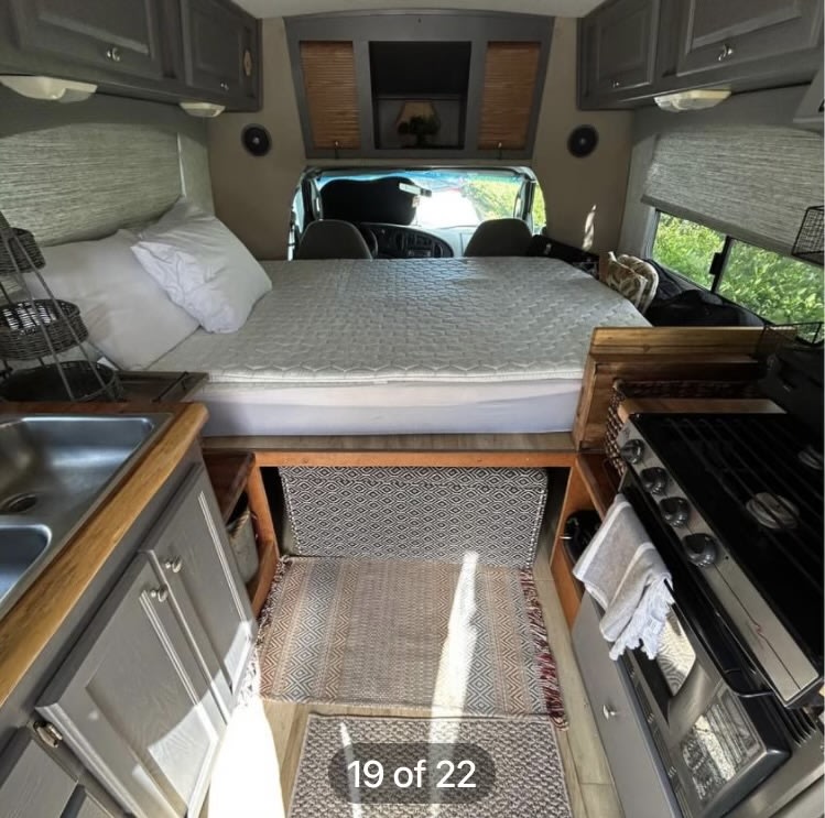 Spacious RV rental interior. Features a cozy bed over the cab, sink, and gas range. Compact travel comfort.. Ford Econoline 2004