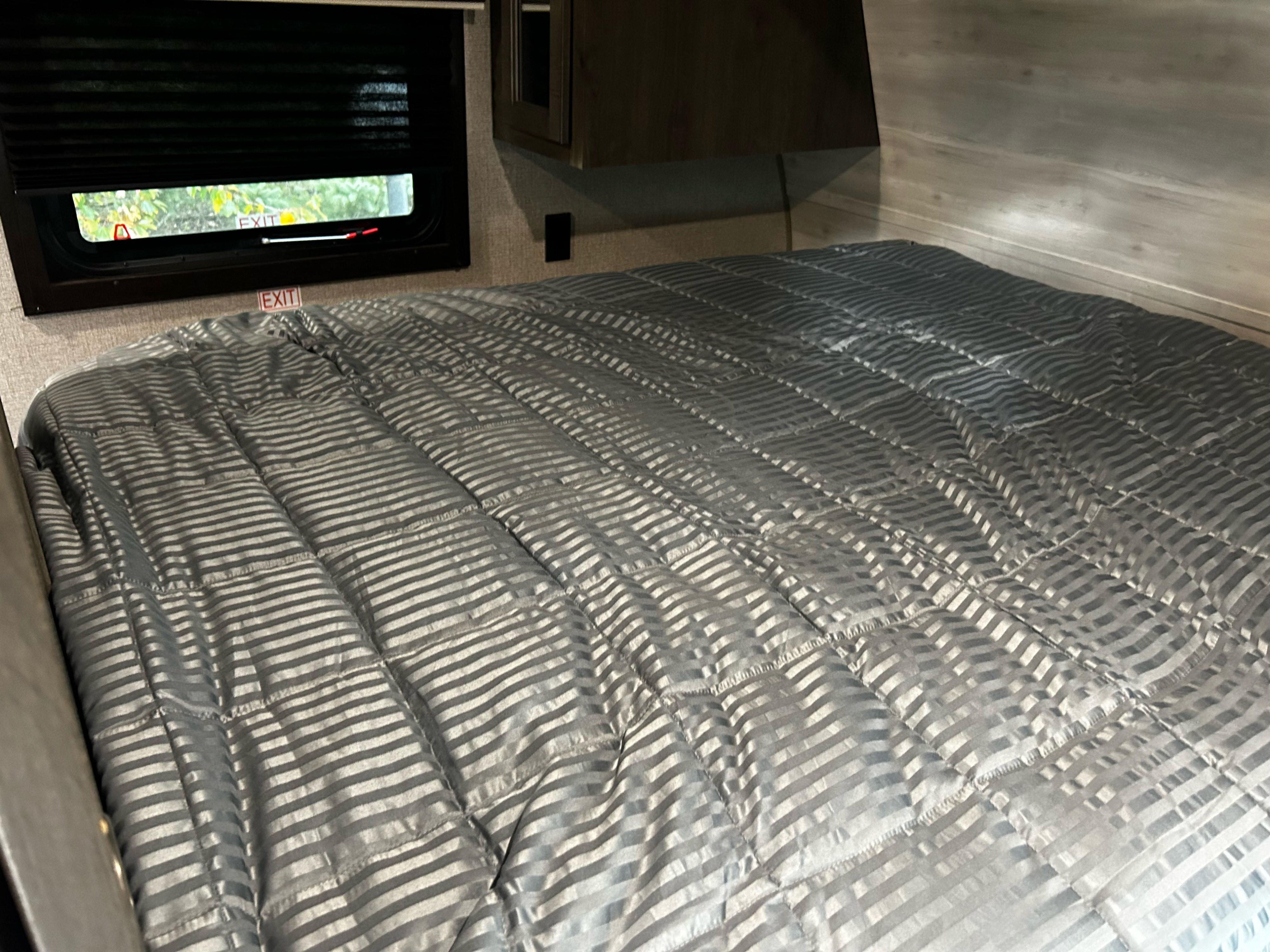 RV rental bedroom interior, showcasing a grey striped bed, exit window, and compact sleeping area.. Jayco Jay Flight 2021