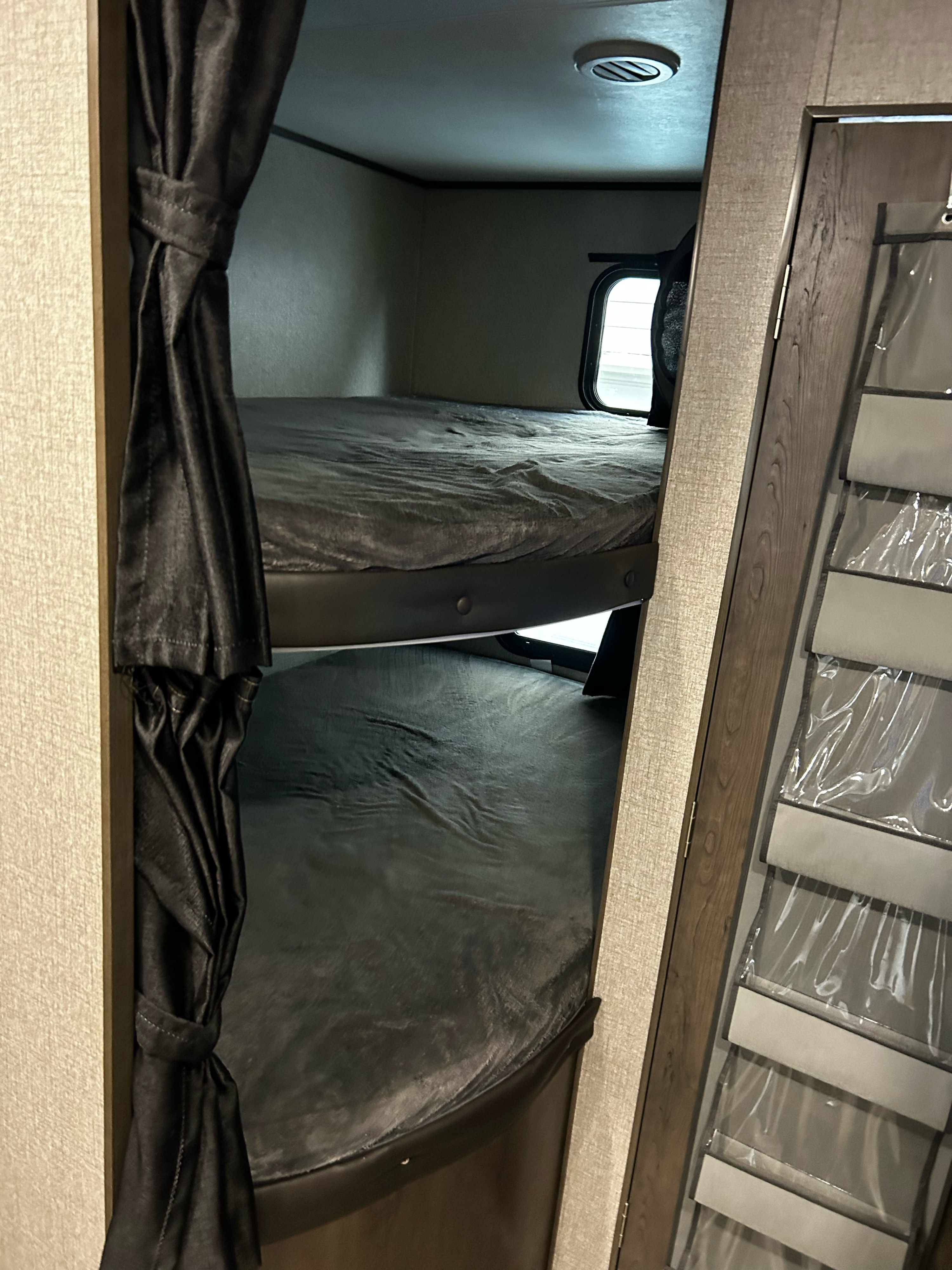 Inside an rv rental, showing two bunk beds with dark curtains and a hanging organizer on the right door.. Jayco Jay Flight 2021