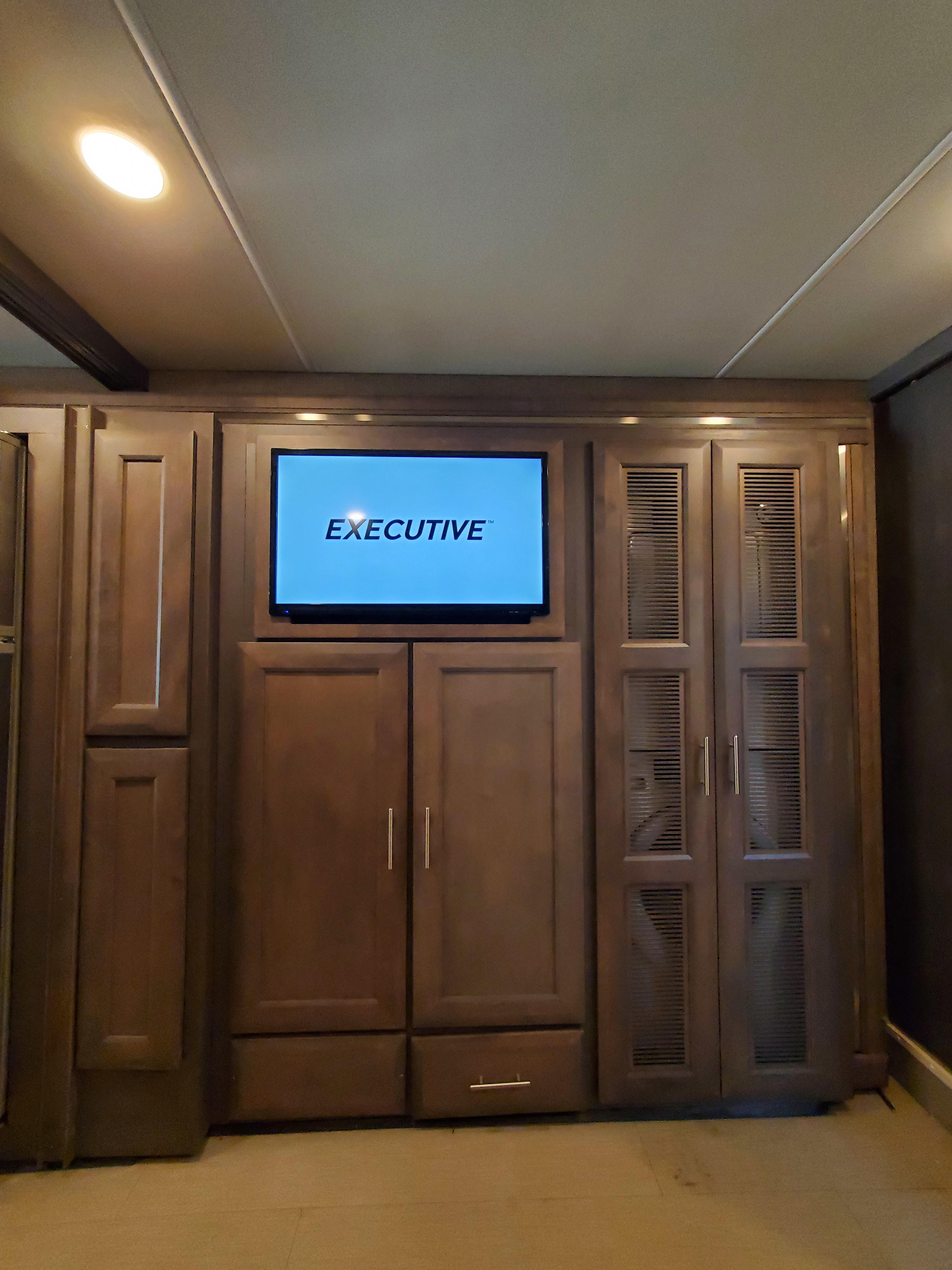 RV rental interior: Built-in wood cabinets frame a TV displaying "EXECUTIVE", offering ample storage.. Thor Palazzo 2022