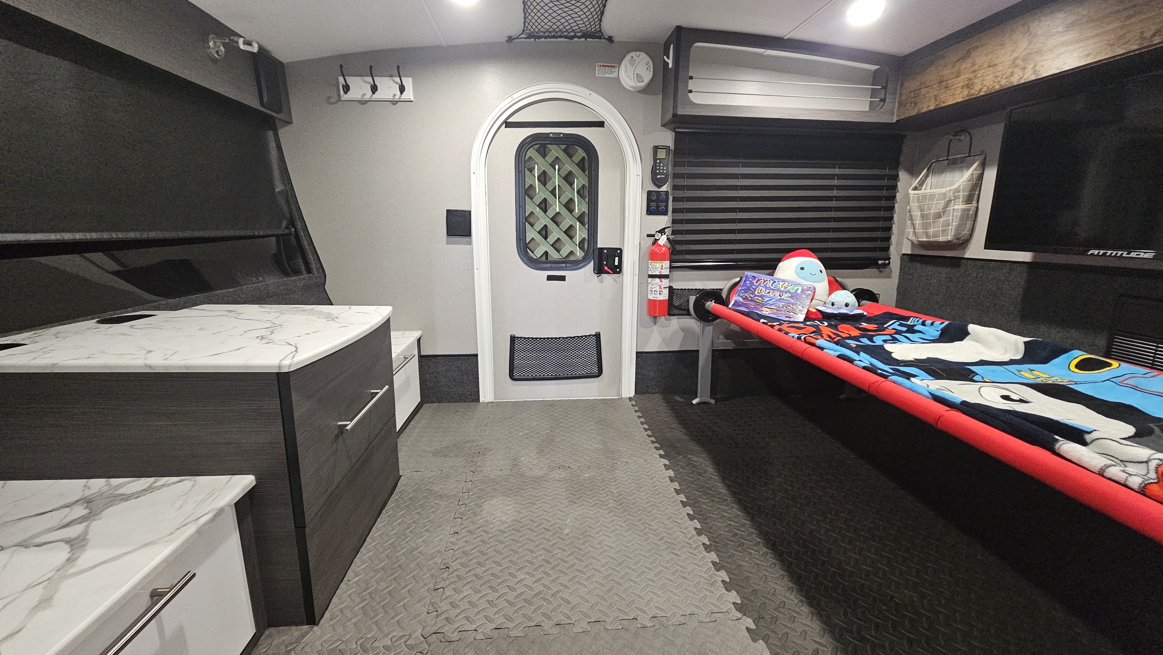 View of a modern RV rental interior, showcasing a child's bunk bed, kitchen counter, and durable toy hauler floor.. InTech Luna 2023