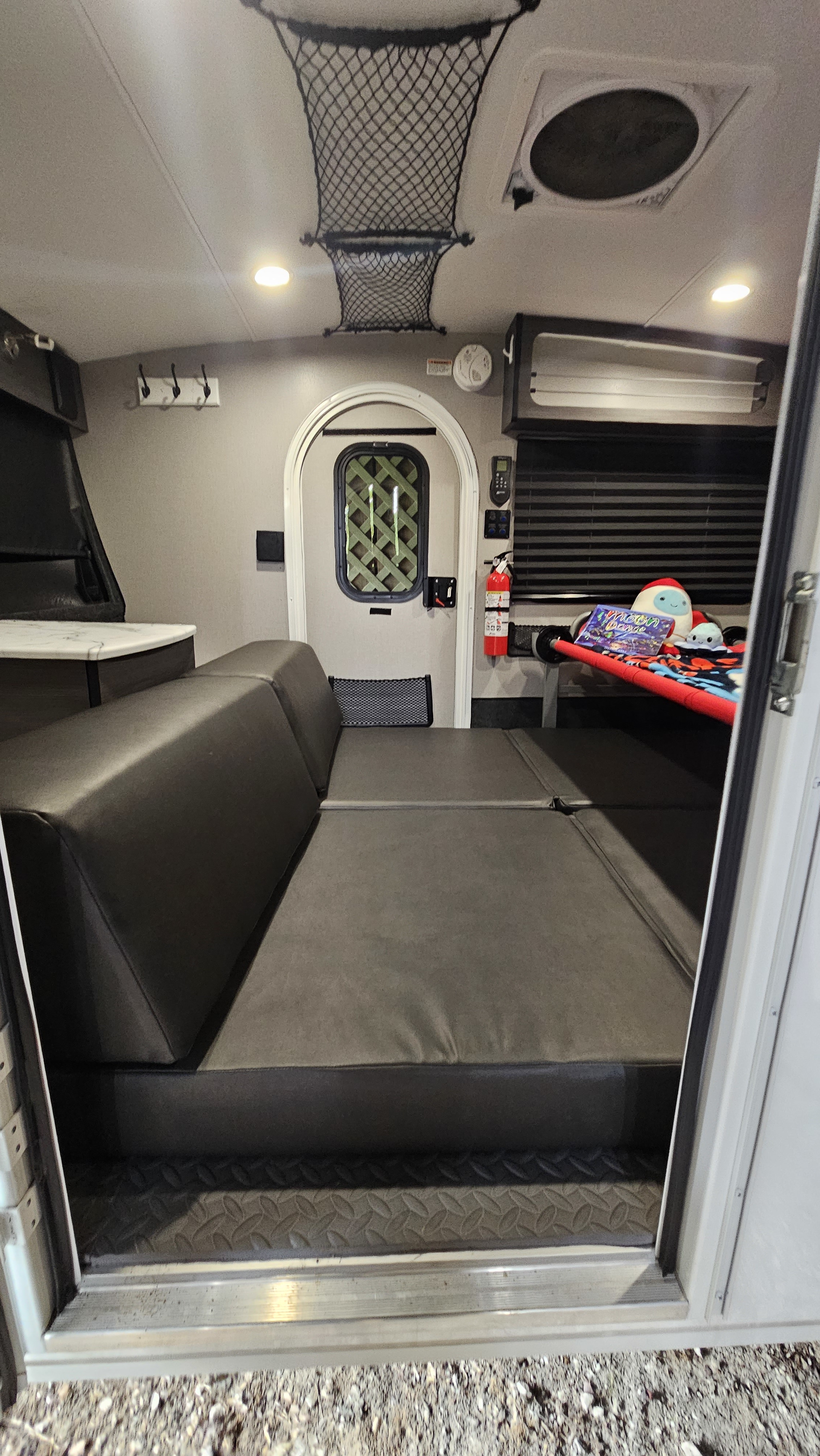 Step inside this RV rental to see its compact living area: dark gray convertible seating, kitchen counter, and a cozy bunk.. InTech Luna 2023