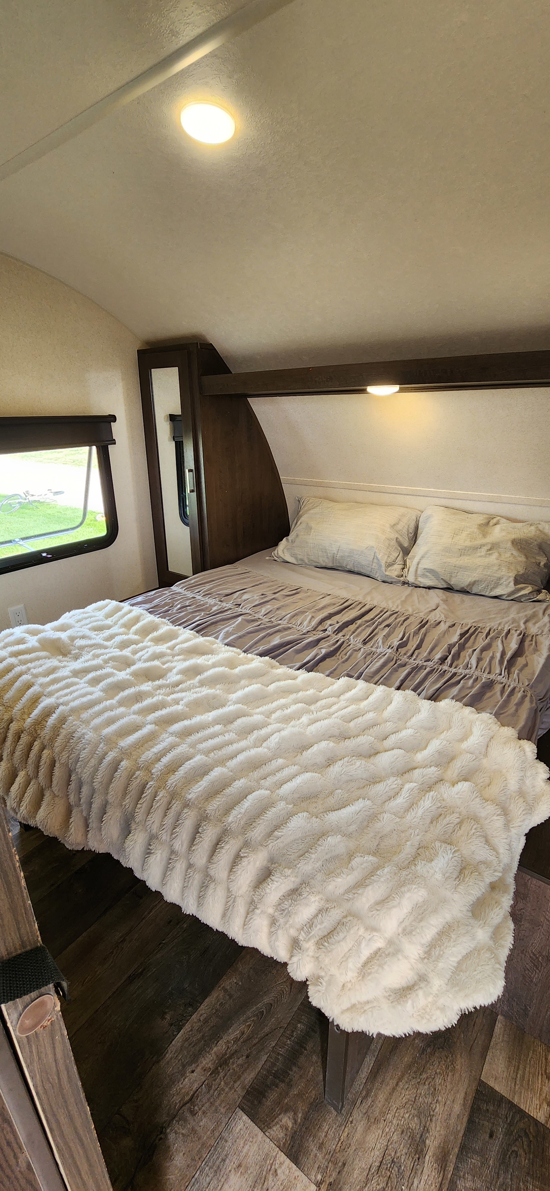 Step inside this comfortable RV rental bedroom, featuring a large bed with a fluffy blanket, wood accents, and a window view.. Forest River Salem Cruise Lite 2018