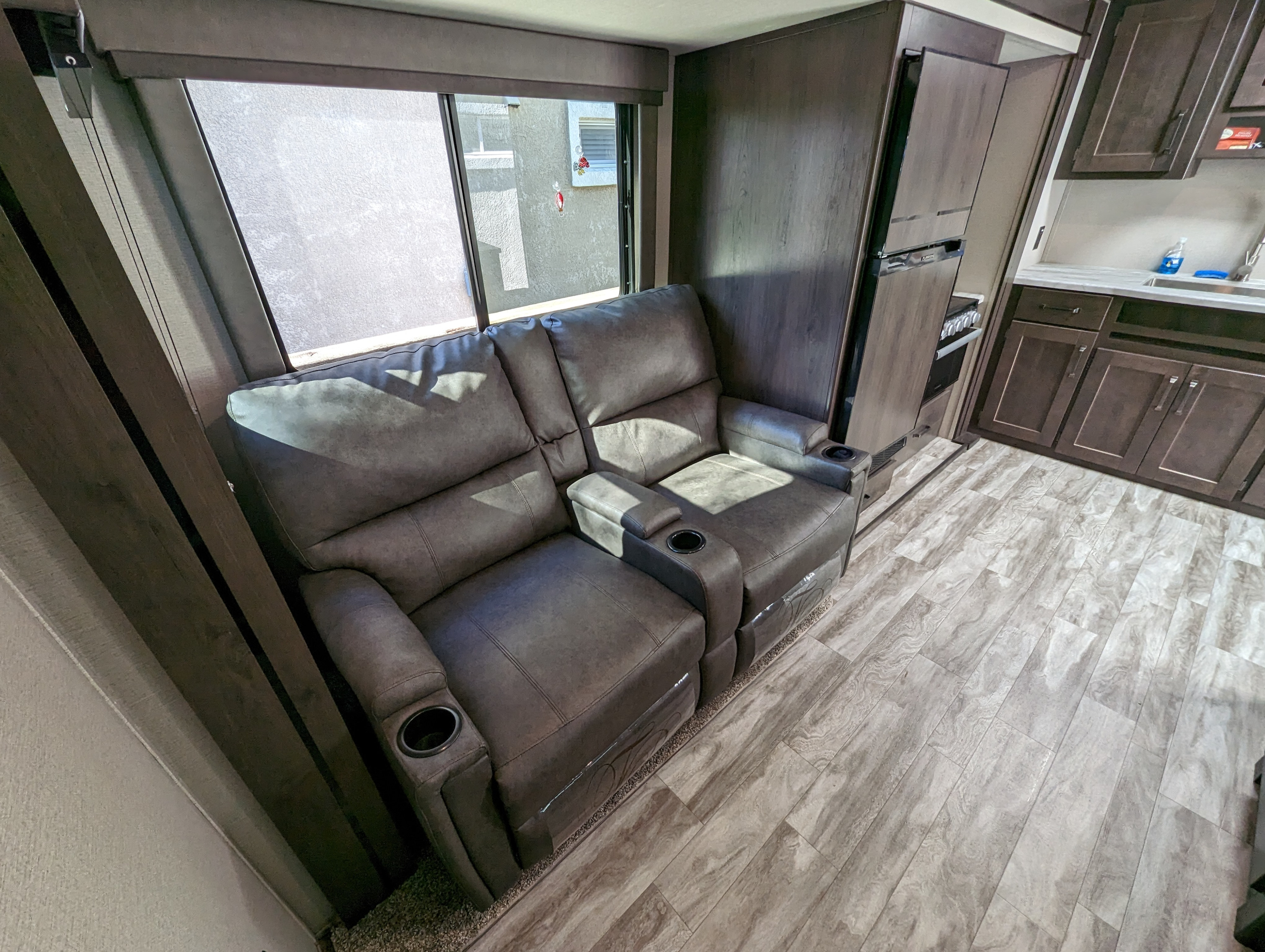 RV rental interior with comfy gray recliners, cup holders, large window, and a compact kitchen area.. Grand Design Transcend Xplor 2022