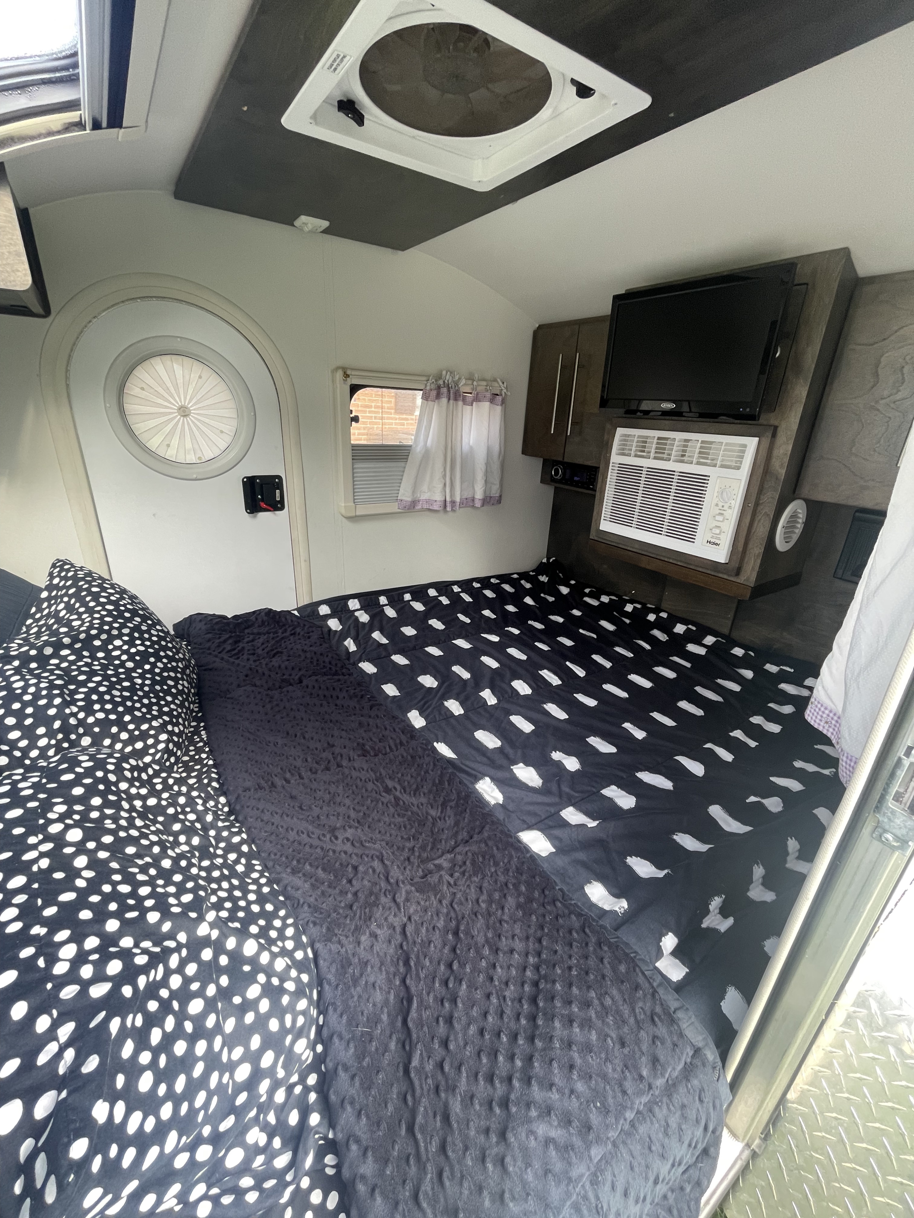 Cozy RV rental interior featuring a patterned bed, mounted TV, AC unit, and a distinctive round door.. nuCamp T@G 2020