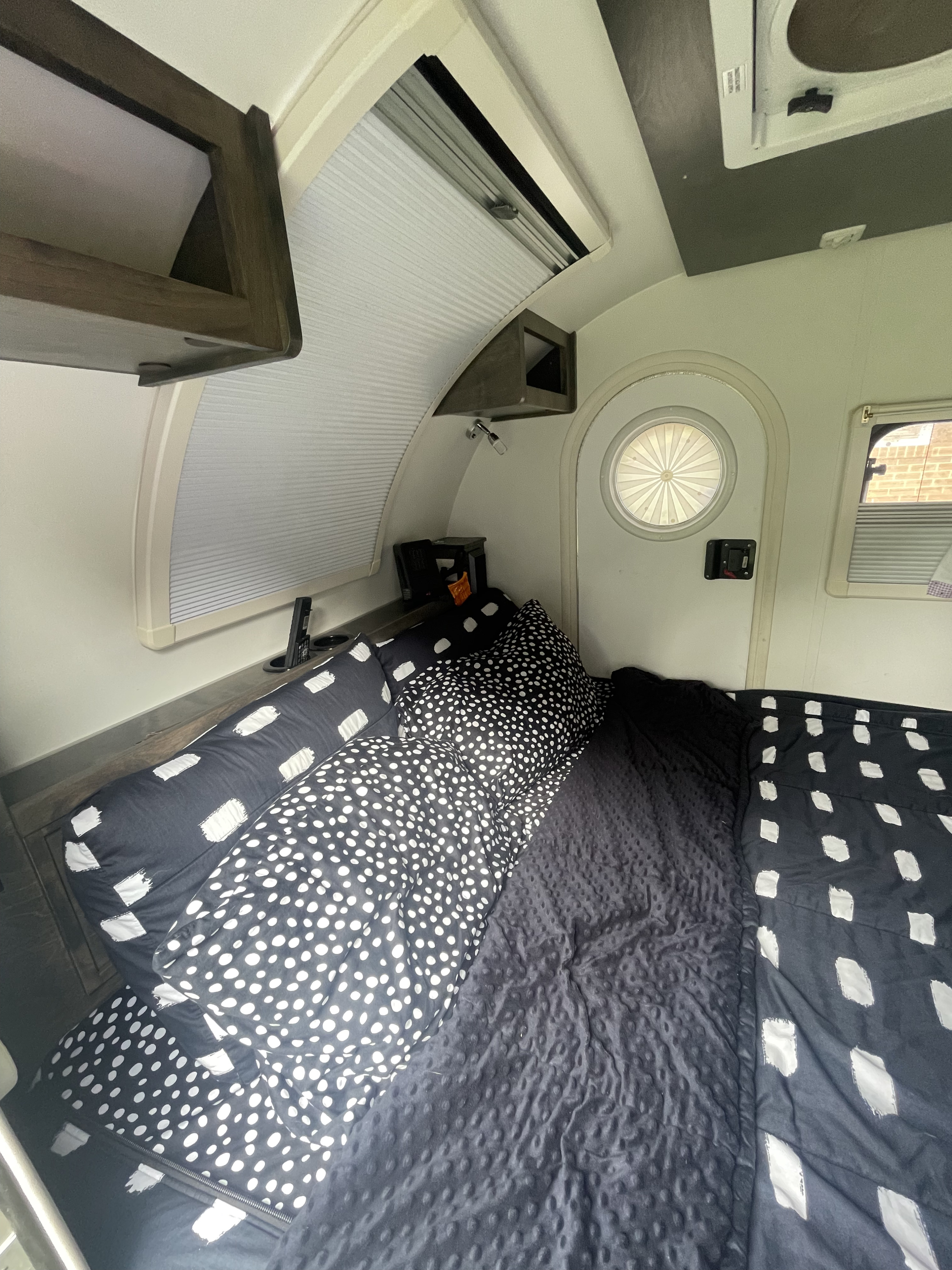 Cozy rv rental bedroom showing a bed with black and white polka dot and brushstroke patterned bedding and windows.. nuCamp T@G 2020