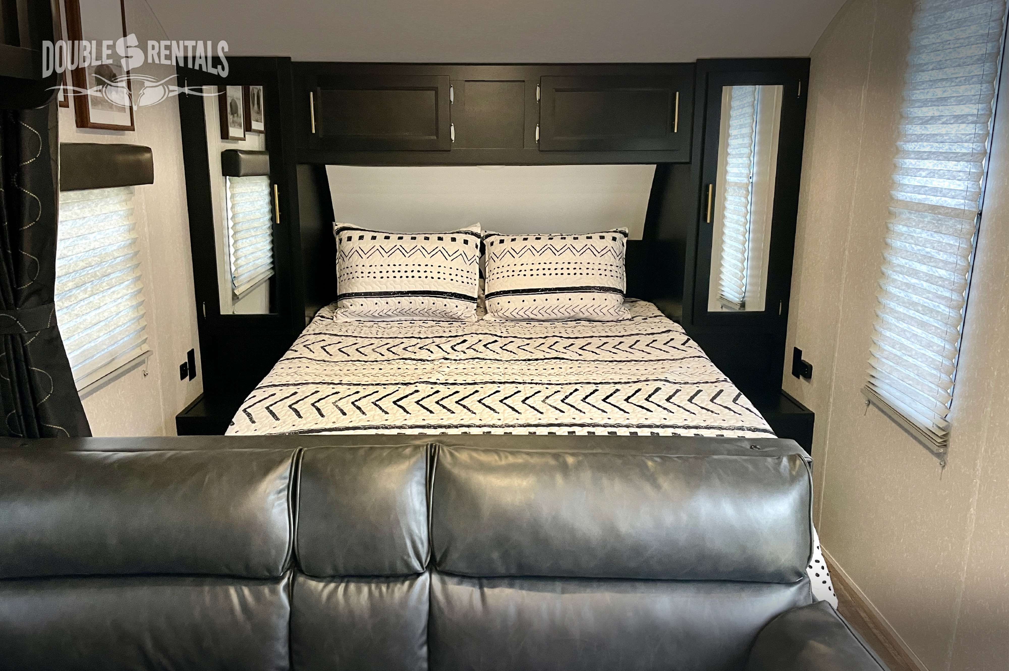 RV rental bedroom: A comfortable bed with patterned linens, overhead cabinets, and mirrored wardrobes. View from a plush sofa.. Forest River Cherokee Grey Wolf 2022