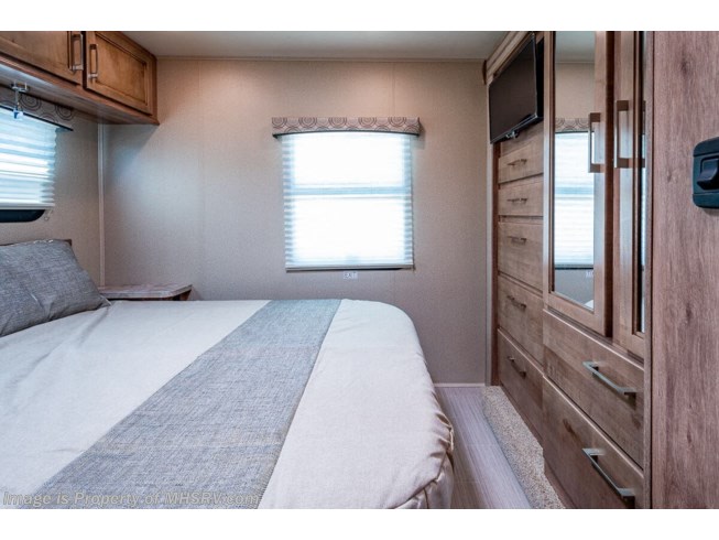 This RV rental bedroom offers a cozy bed, window, and wood-toned wardrobe with TV, creating a comfortable travel space.. Jayco Entegra Odyssey 2020