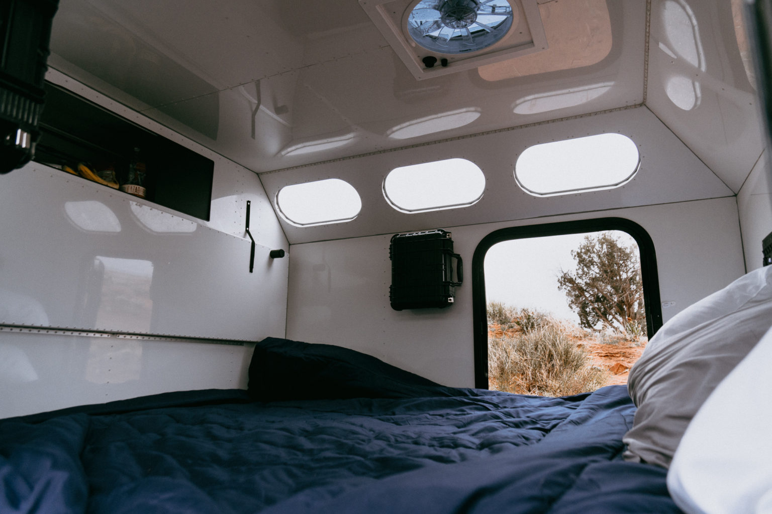 RV rental: Inside a sleek camper with a comfortable bed, overhead fan, storage, and a window framing a desert landscape.. Mammoth Overland HV 2023