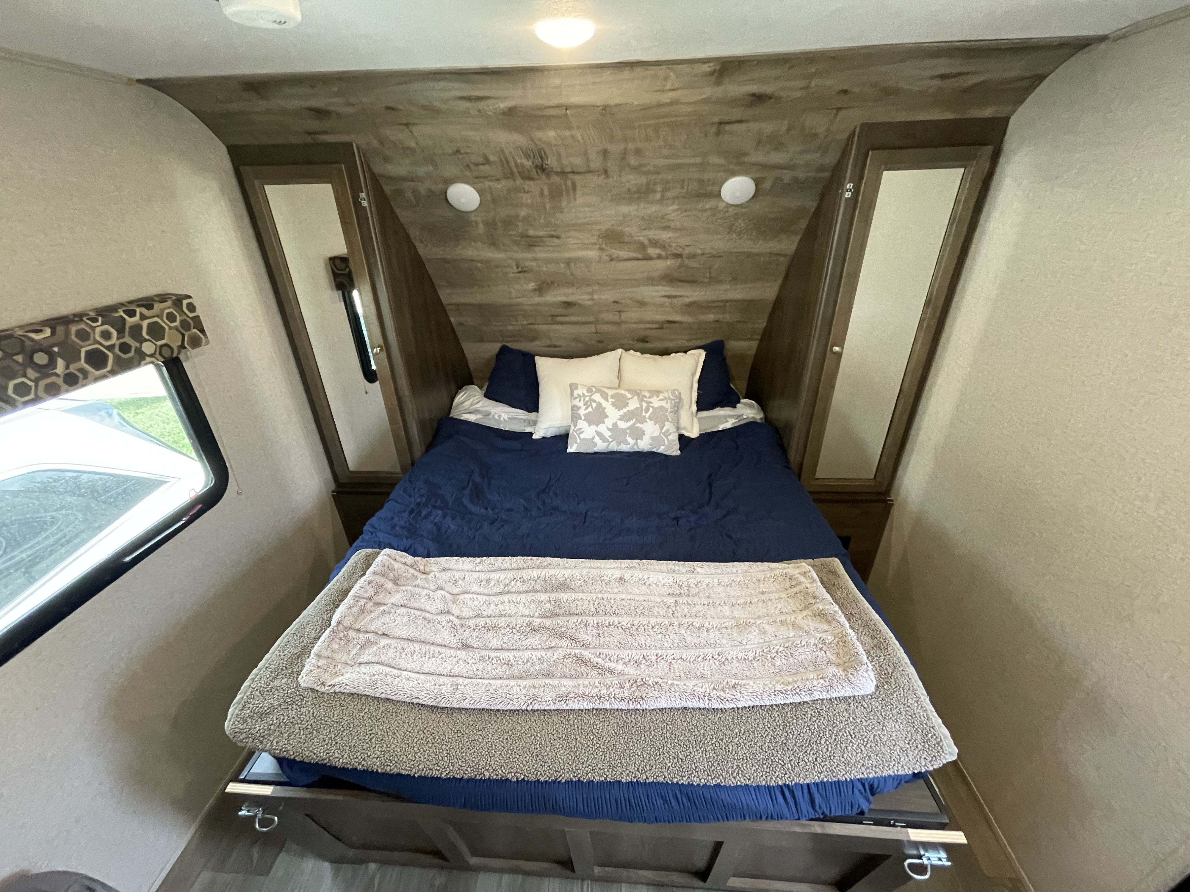 RV rental bedroom: cozy space with a bed, blue comforter, blankets, wood-paneled walls, and built-in cabinets.. Dutchmen Coleman Light LX 2019