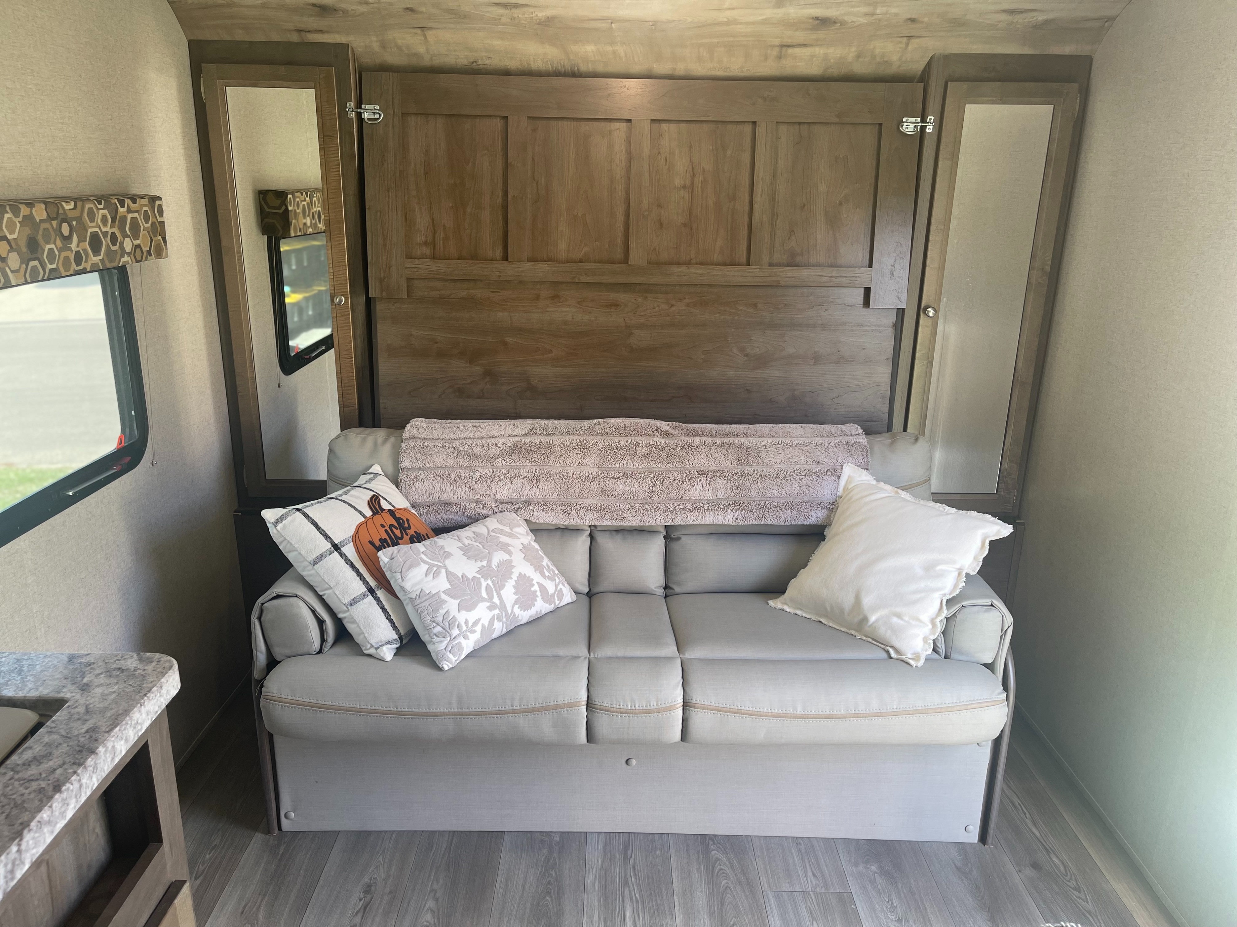 RV rental interior featuring a comfortable sofa with decorative pillows, a wooden murphy bed, and mirrored cabinets.. Dutchmen Coleman Light LX 2019