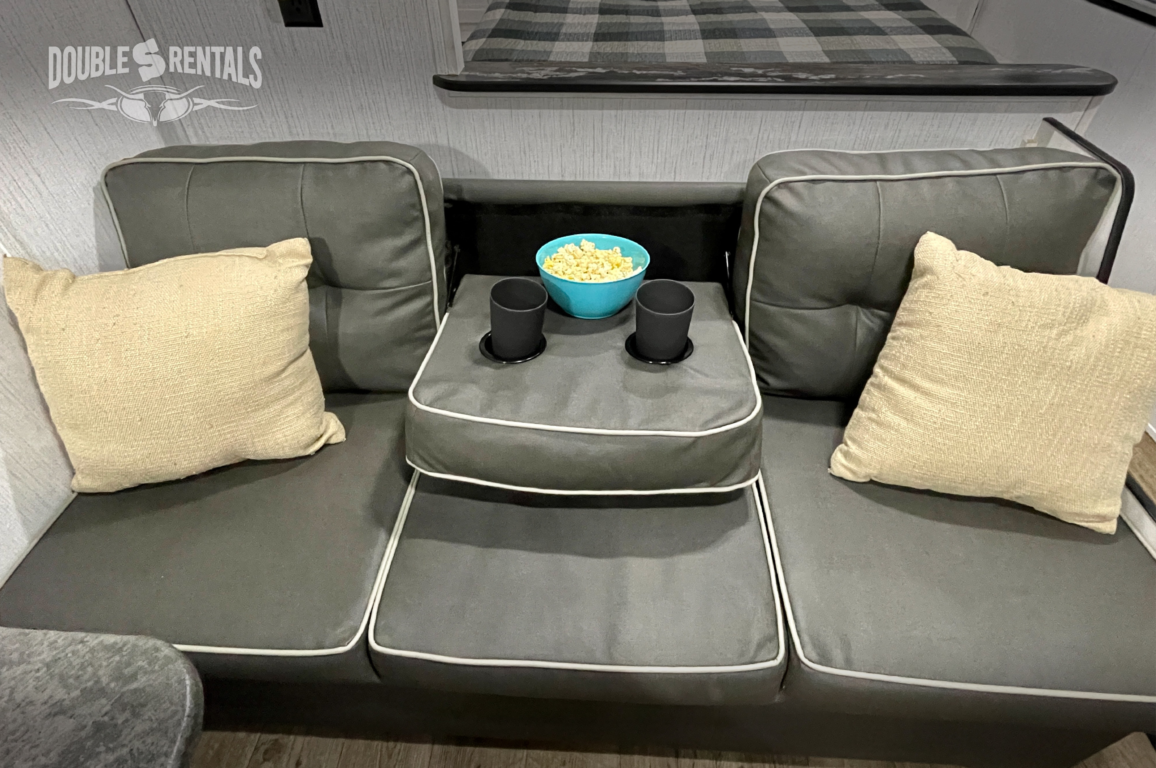 Cozy RV rental couch with popcorn, perfect for movie nights. Features cup holders and comfortable seating.. Heartland Trail Runner 2021