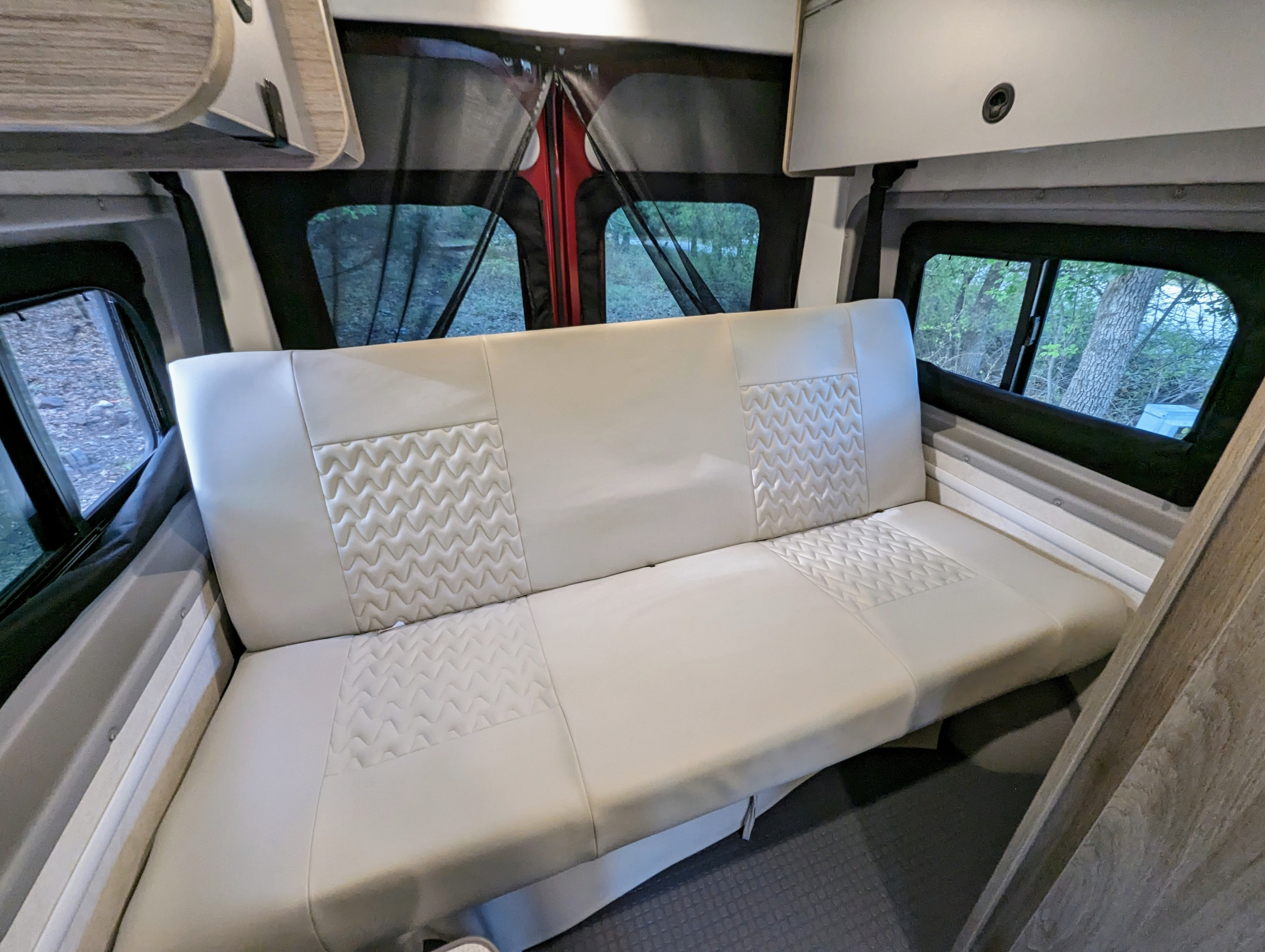 Cozy rv rental interior featuring a patterned bench seat, overhead compartments, and rear windows with mesh.. Winnebago Solis 2023