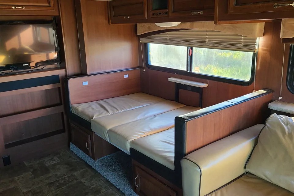 Inside an RV rental: a cozy living area with a convertible dinette bed, TV, and window views.. Fleetwood Bounder Classic 2012