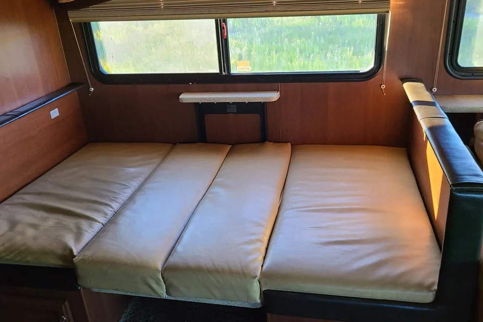 This RV rental features a cozy sleeping area made from tan cushions, a converted dinette by large windows.. Fleetwood Bounder Classic 2012