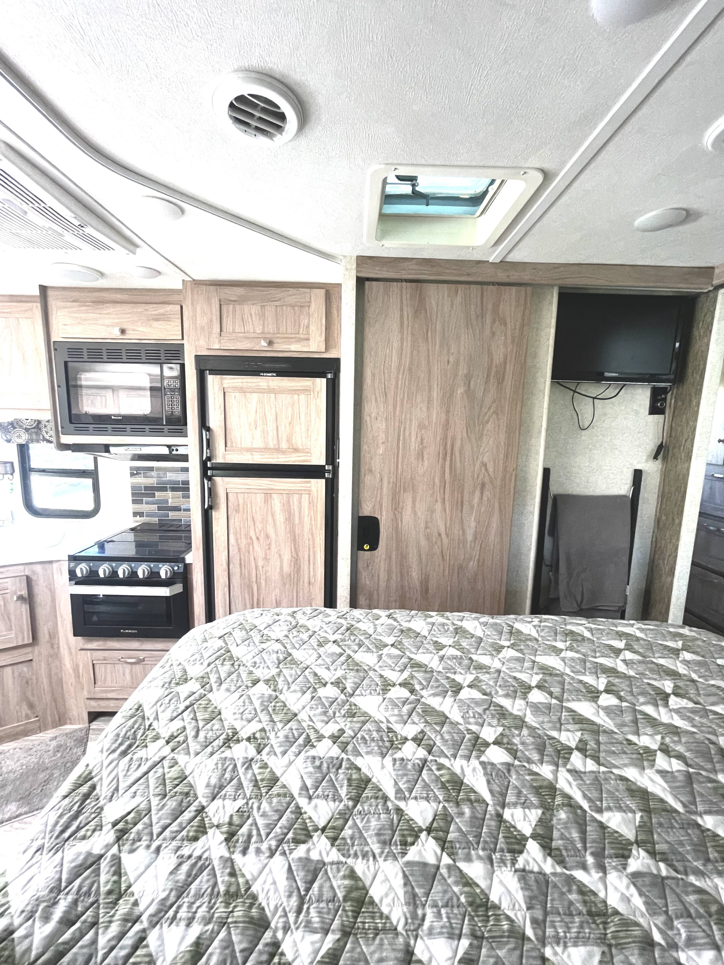 Interior of an RV rental: Bed with quilt, compact kitchen (microwave, stove), refrigerator, TV, and storage.. Forest River Sunseeker 2019