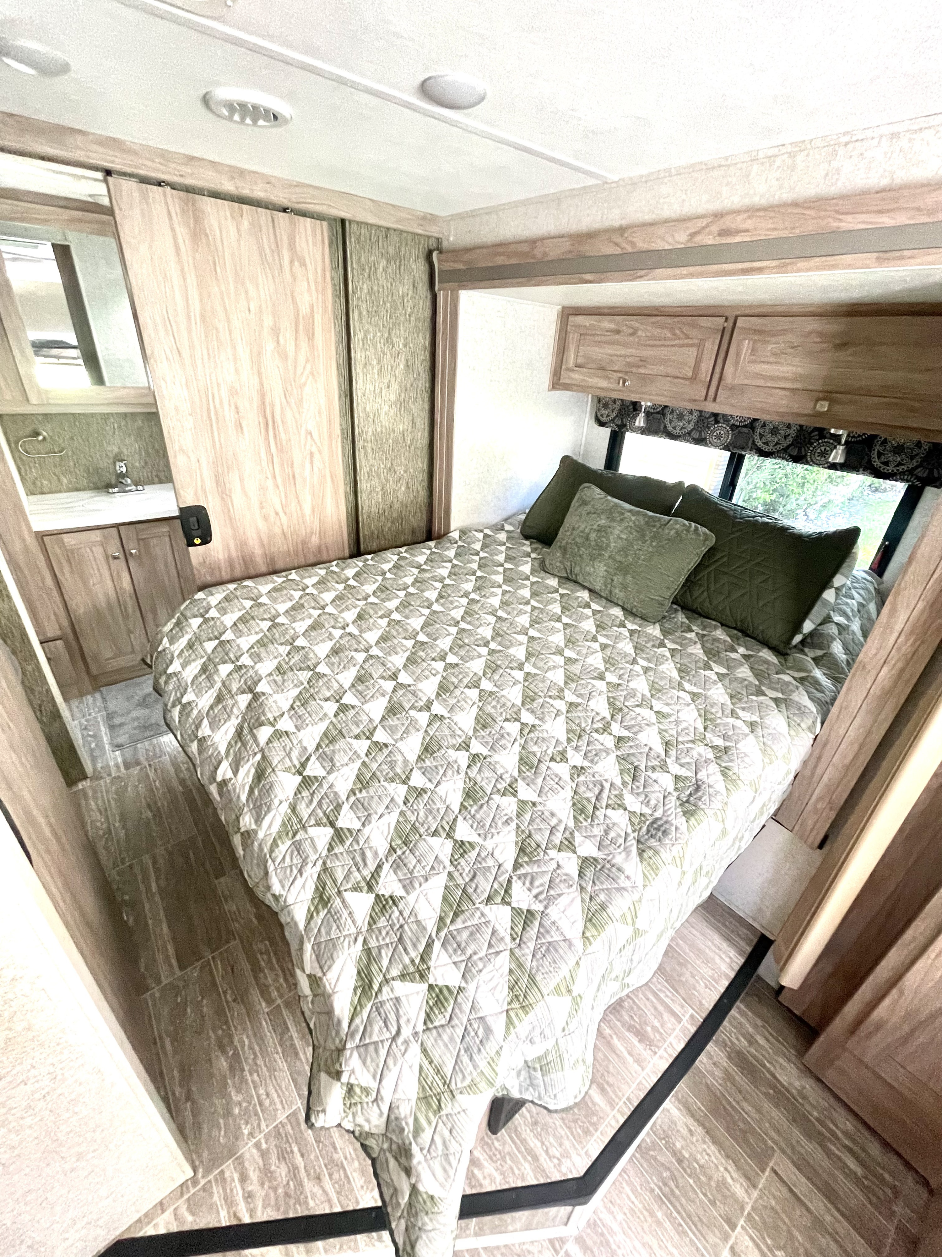 Cozy RV rental bedroom features a quilted bed, overhead cabinets, tiled floor, and a sliding door leading to the vanity.. Forest River Sunseeker 2019