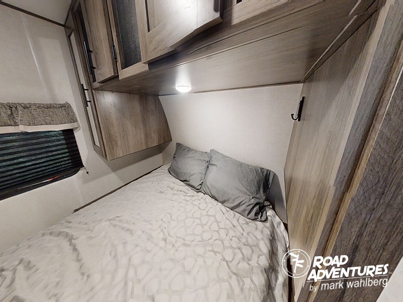 Explore a comfortable RV rental bedroom featuring a bed, overhead storage, and window with blinds.. Prime Time Avenger 24BHS 2021