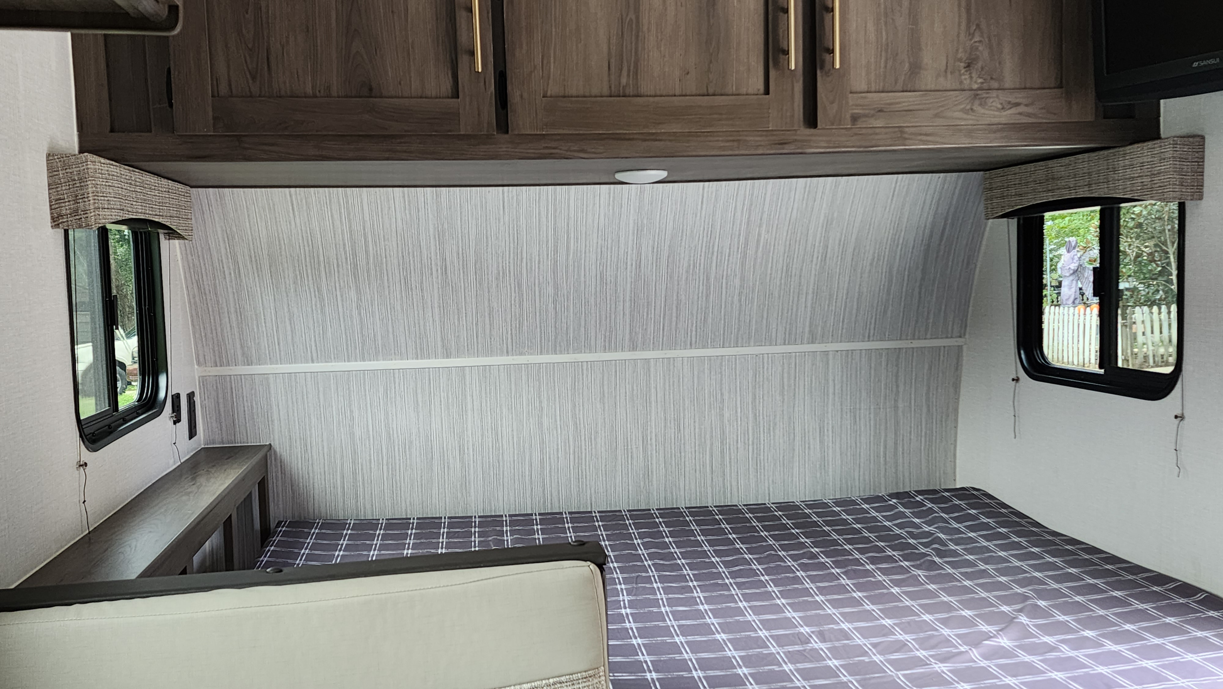 RV rental bedroom with a comfy bed, wooden overhead cabinets, and a side bench. Large windows offer outdoor views.. Forest River Viking Ultra Lite 2022