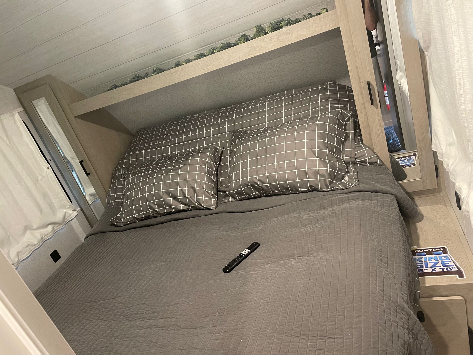 Cozy RV rental bedroom featuring a custom king-size bed with grey bedding and a remote control for comfort.. Forest River Wildwood X-Lite 2024