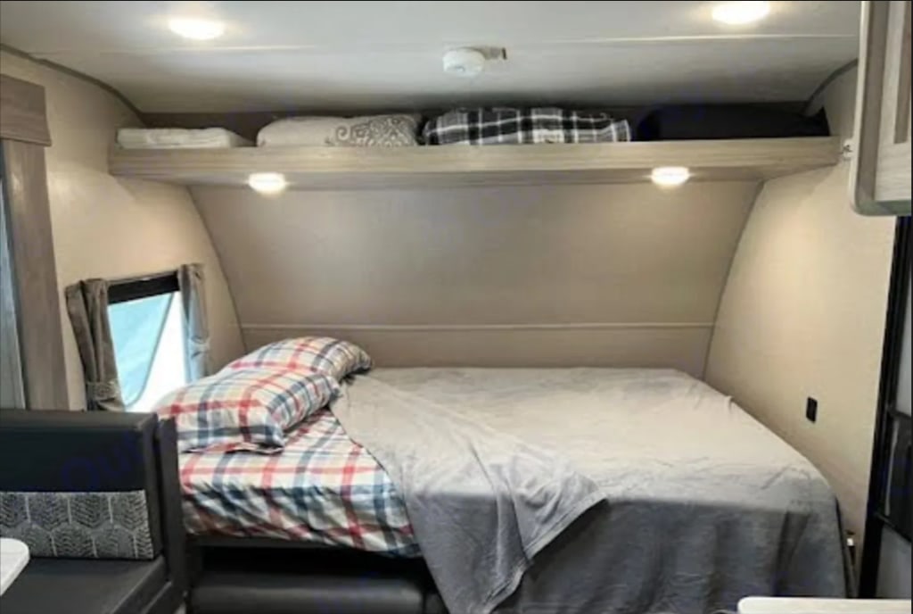Inside a clean RV rental, featuring a neatly made bed, overhead storage shelf, and a window for natural light.. Coachmen Catalina Summit 2022