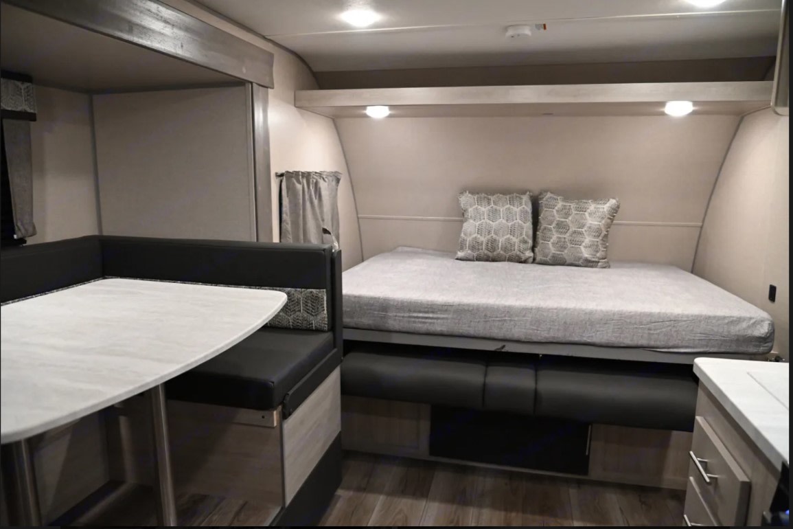 RV rental interior: a compact space with a black booth dinette, a light-colored table, and a bed with grey bedding and pillows.. Coachmen Catalina Summit 2022