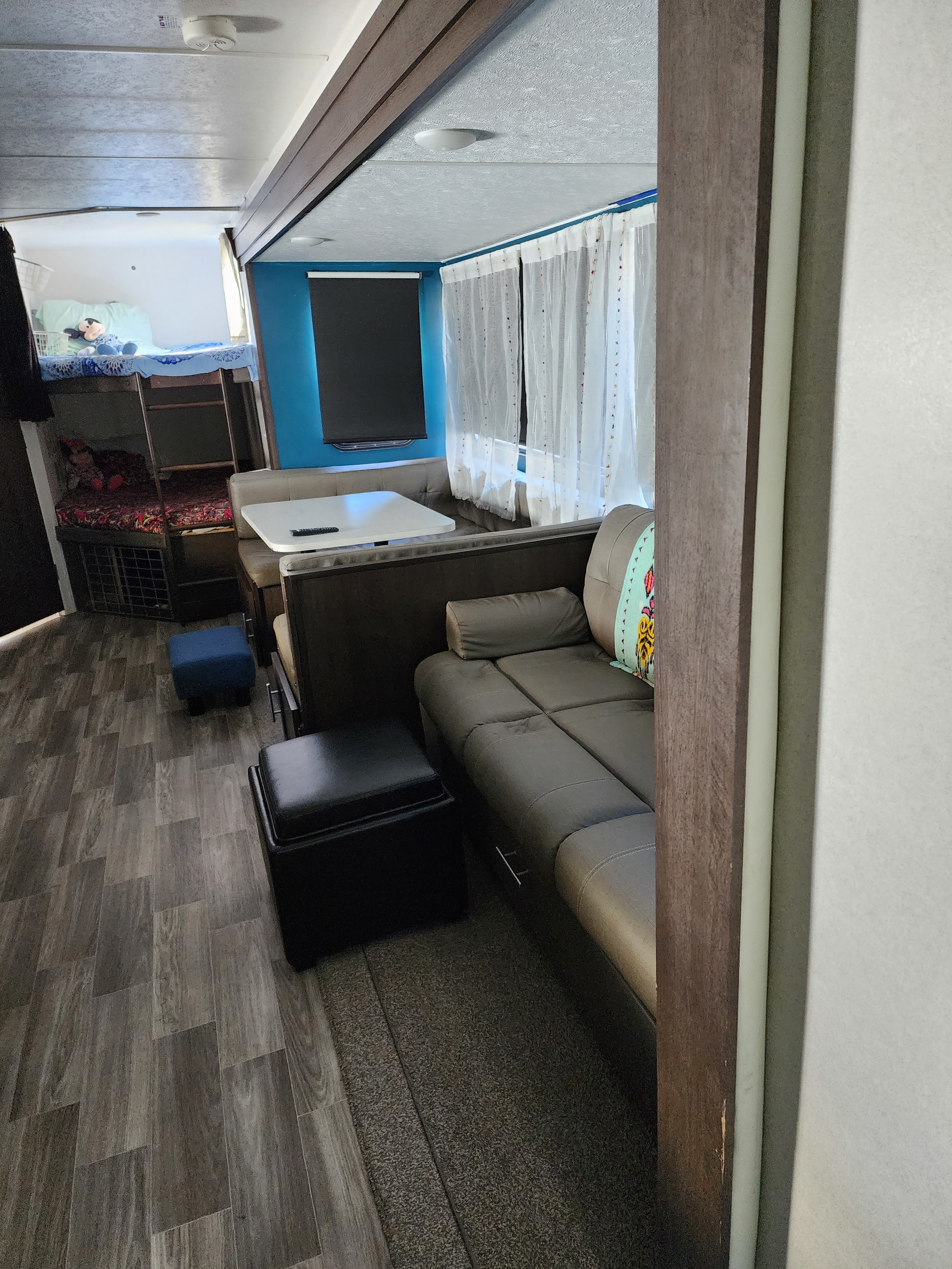 Modern rv rental interior: view of dining booth, sofa, and bunk bed area, featuring stylish wood-look flooring.. Forest River Wildwood 2019