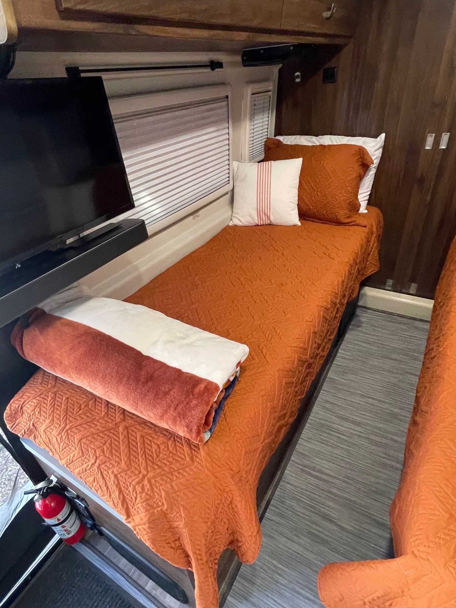 Cozy RV rental bedroom with twin beds featuring orange quilts, pillows, and a TV.. Winnebago Travato 2023