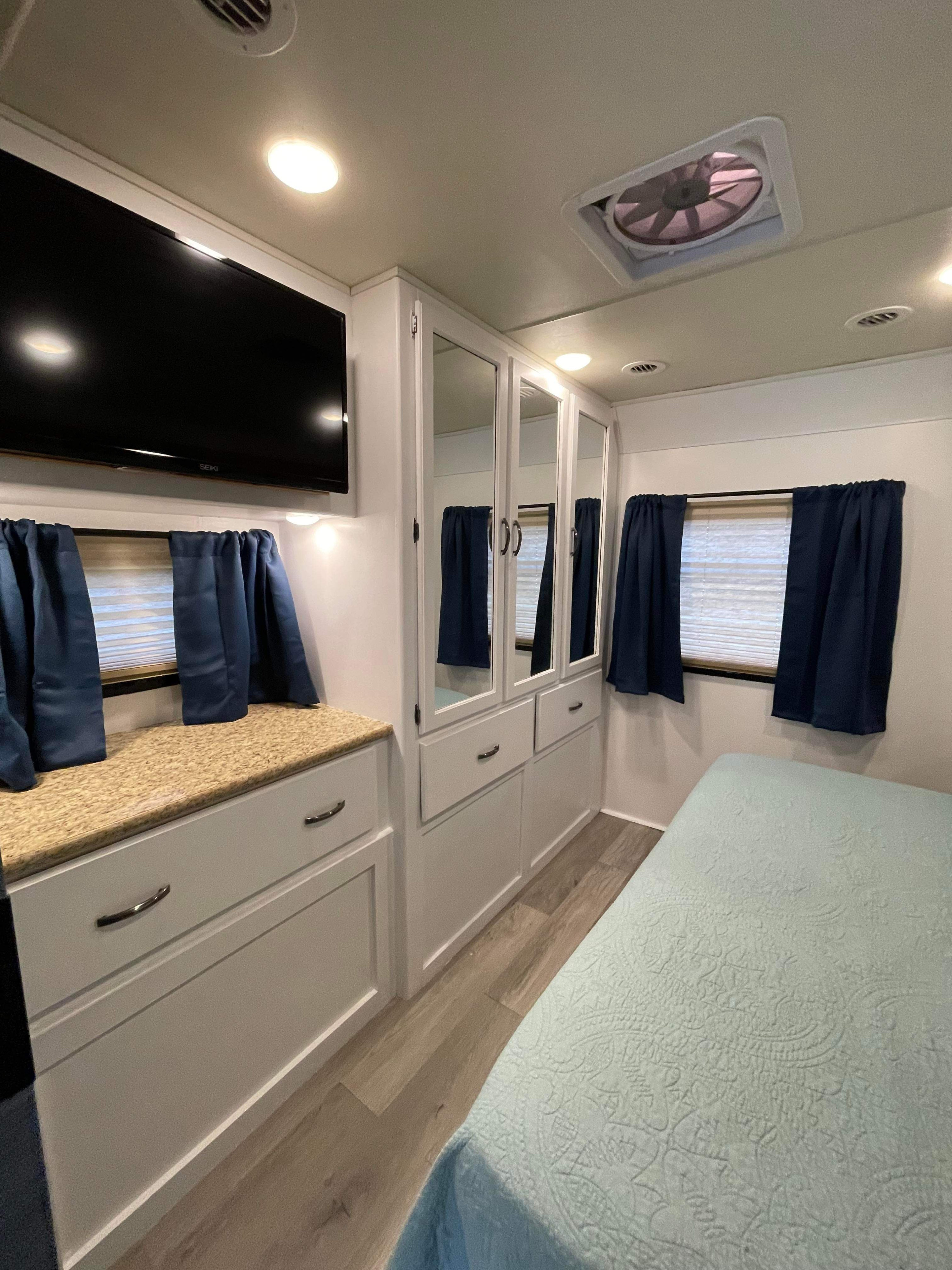 Cozy RV rental bedroom: features a comfortable bed, mounted TV, mirrored cabinets, and ample storage. Perfect for adventurers.. Thor A.C.E. 2016