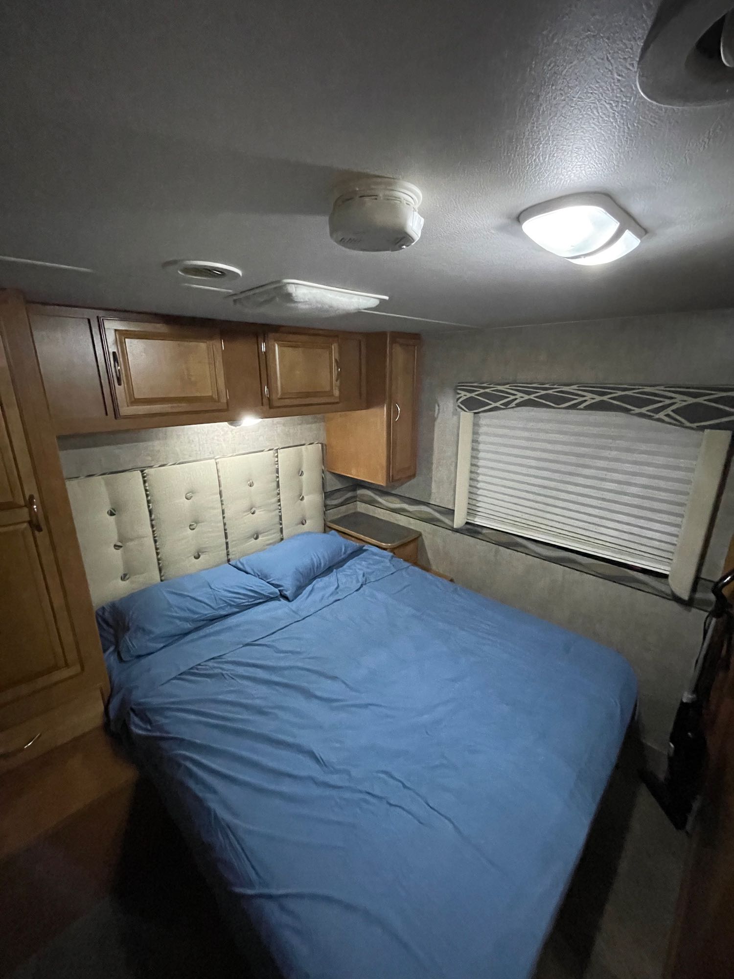 Cozy RV rental bedroom: Features a comfy bed with blue sheets, built-in cabinets, and window. Perfect for your mobile adventures.. Winnebago Minnie Winnie 2016