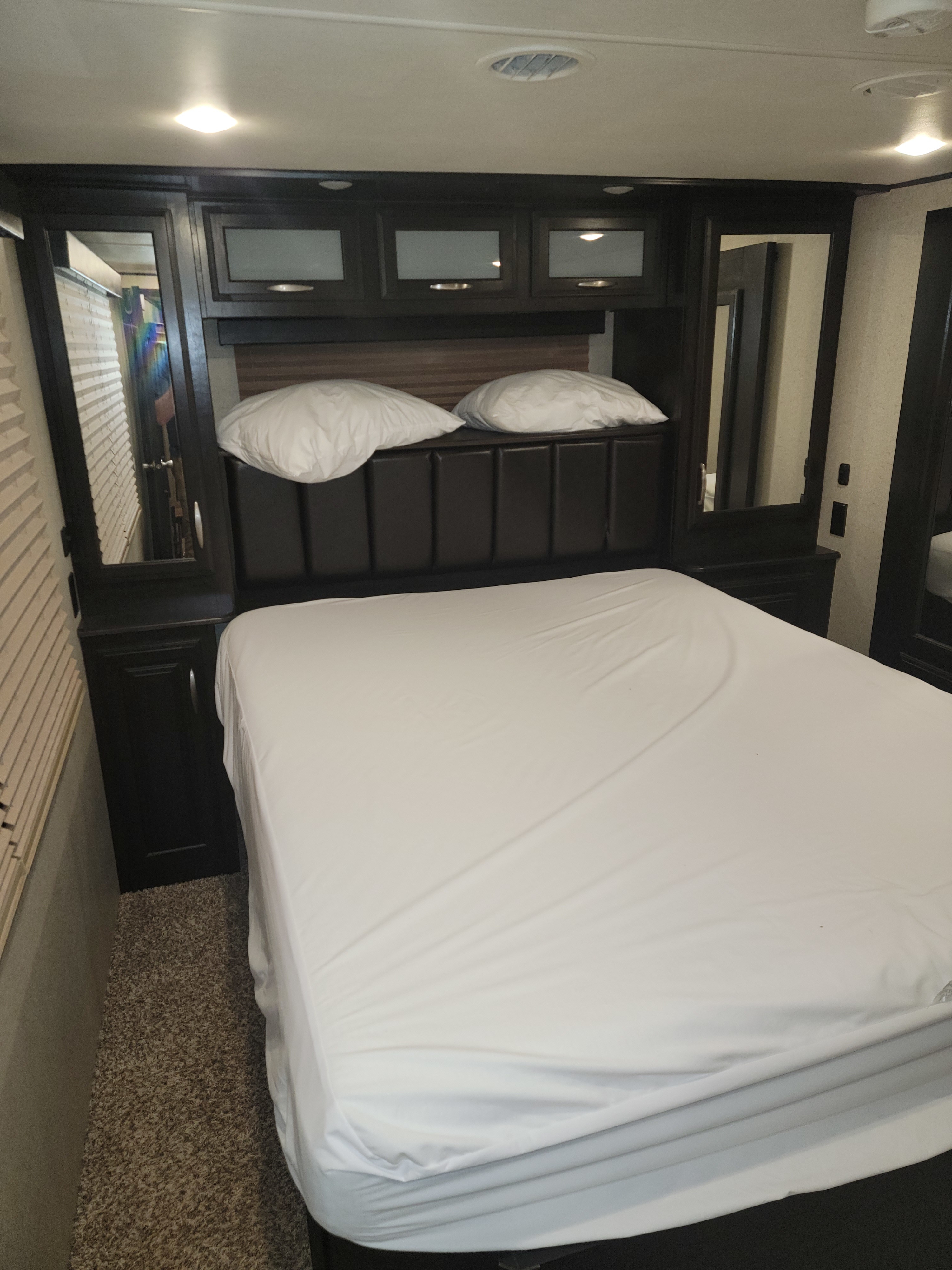 RV rental bedroom: a comfortable space with a bed, dark headboard, and overhead cabinets.. Grand Design Momentum Toy Hauler 2018
