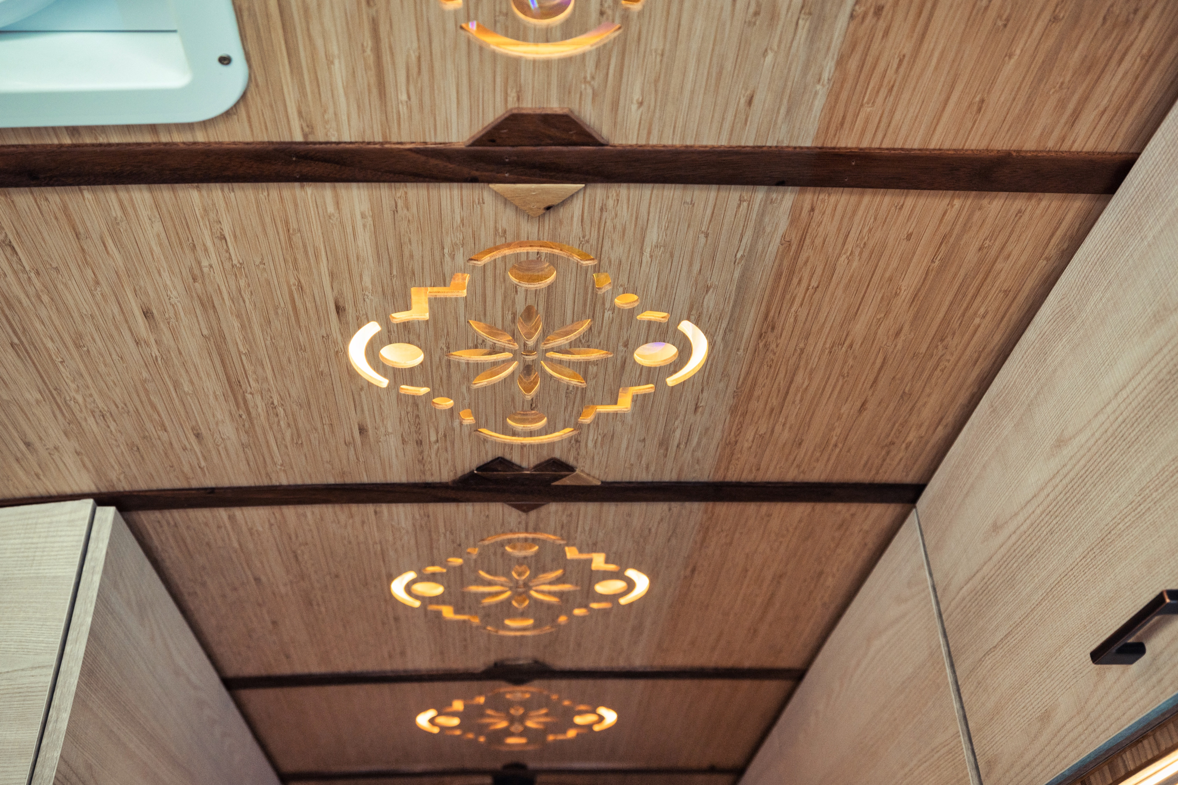 Warm wooden ceiling of an RV rental, featuring intricate cut-out lights and a dark accent beam. Modern camper interior design.. Mercedes-Benz Sprinter 2022