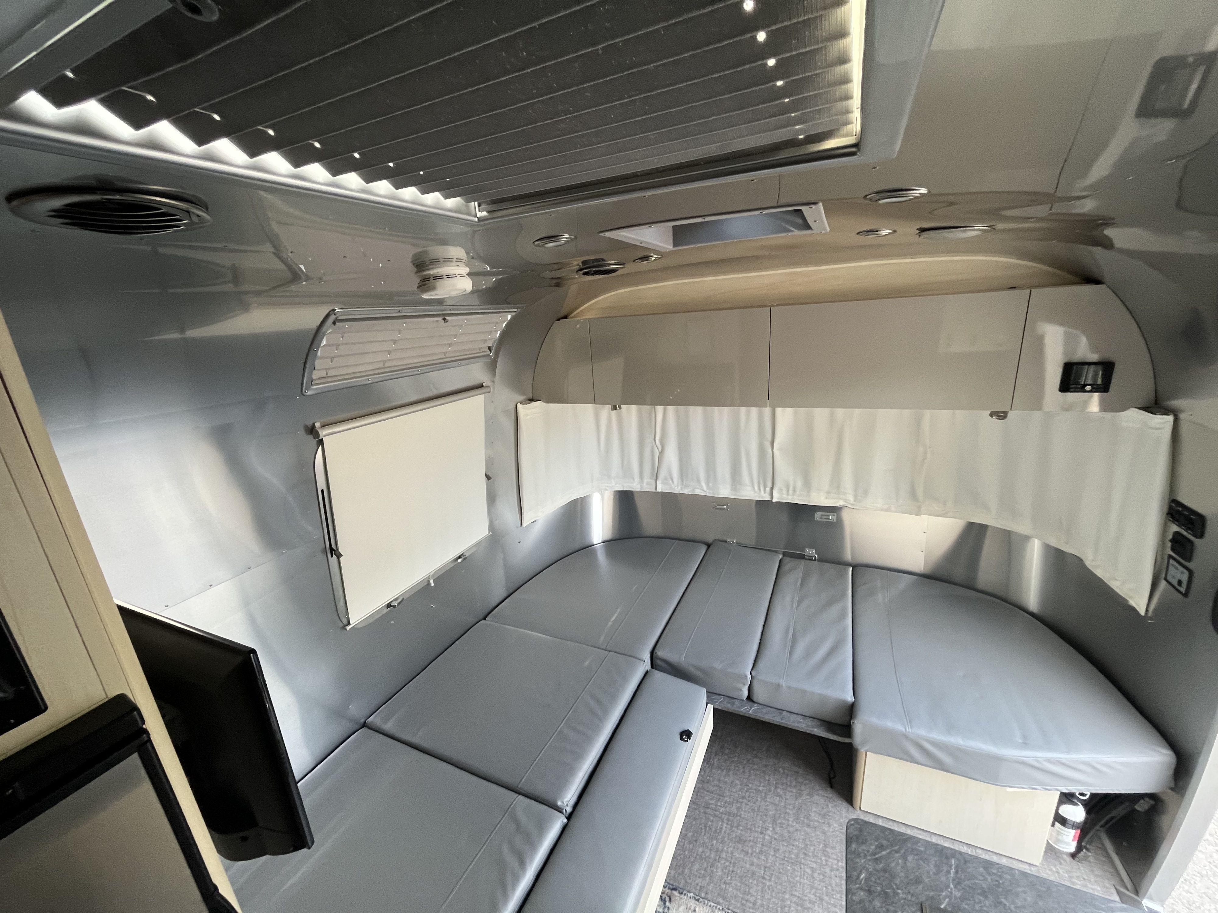 This well-lit RV rental interior features comfortable grey U-shaped seating, sleek aluminum walls, and practical storage.. Airstream Flying Cloud 2021