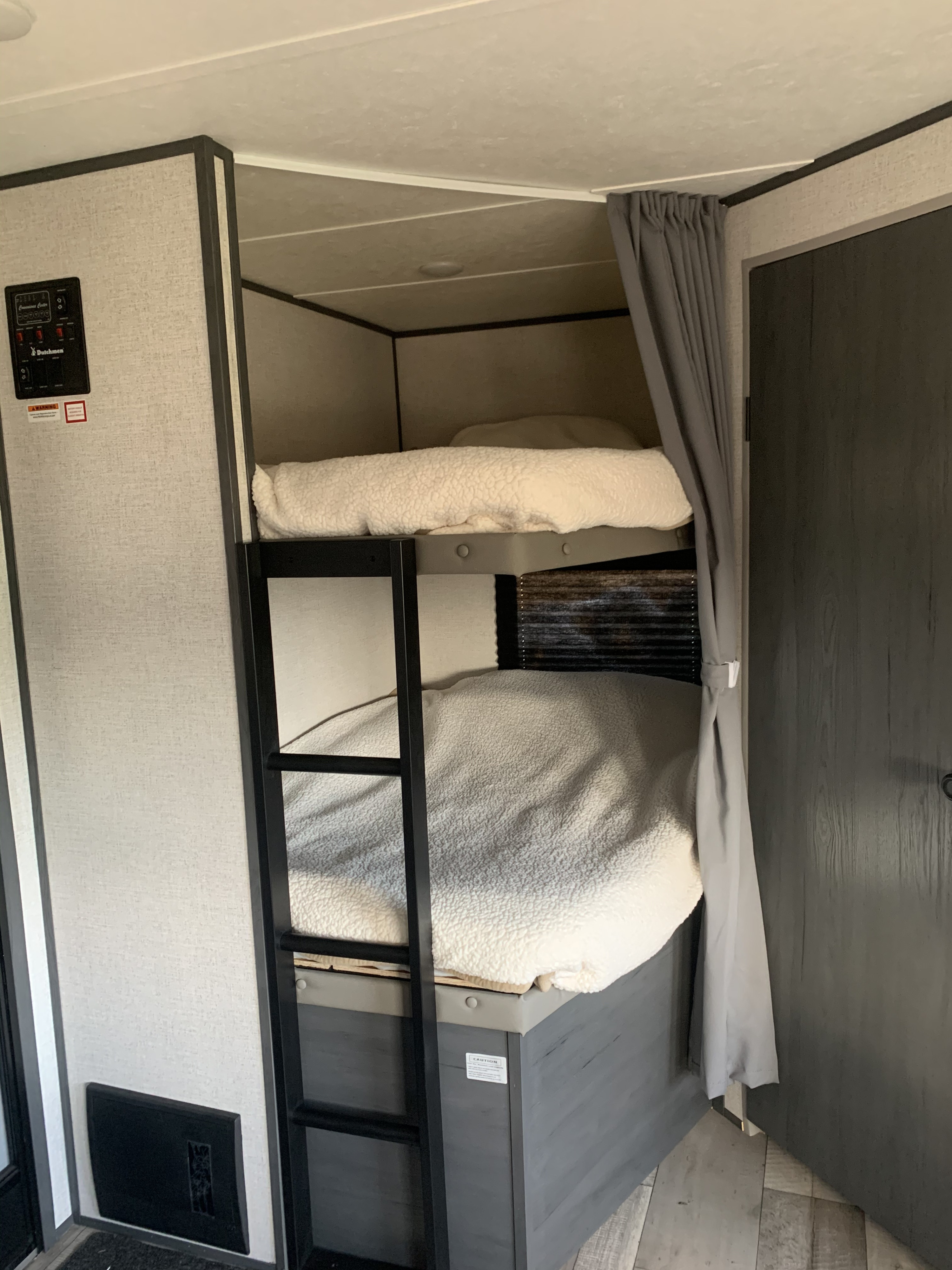Cozy RV rental interior: stacked bunk beds with fluffy white blankets, a ladder, and a grey privacy curtain for travelers.. Dutchmen Other 2021