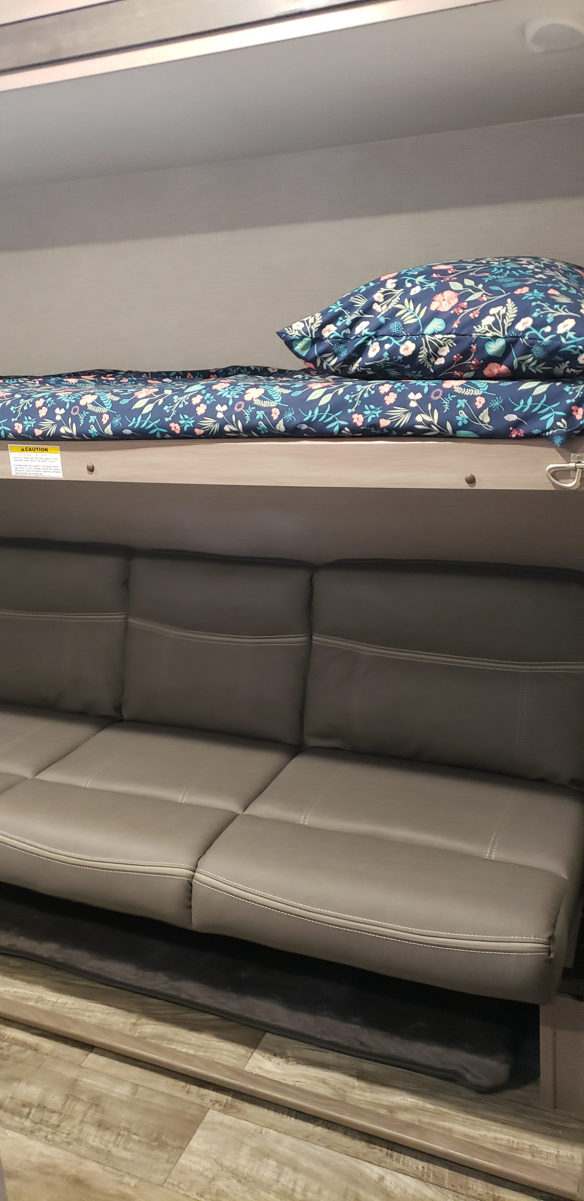 Inside an RV rental: a floral bunk bed above a grey faux leather sofa, providing comfortable sleeping and seating options.. Keystone RV Sunset Trail 2022