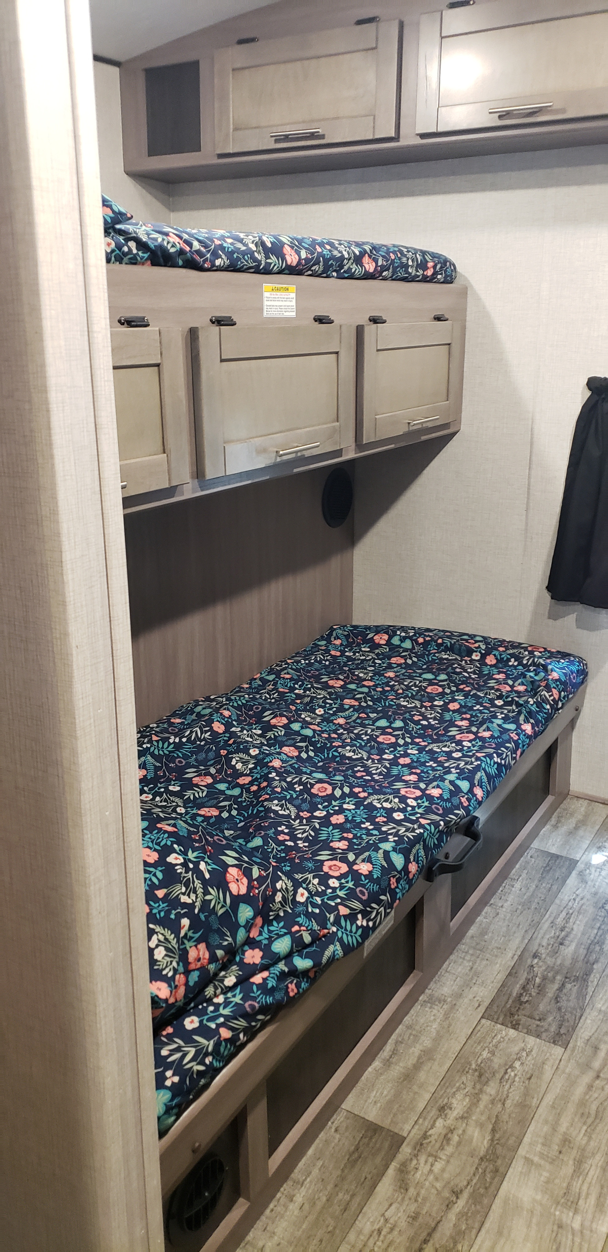 RV rental bunk beds feature colorful floral bedding in this compact sleeping area, with overhead storage and wood-look flooring.. Keystone RV Sunset Trail 2022