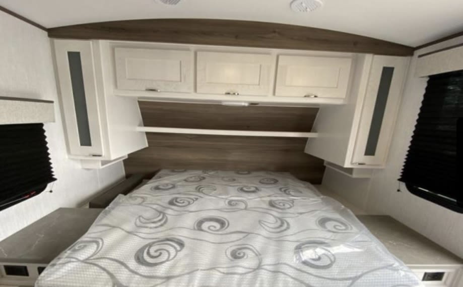 Spacious RV rental bedroom features a comfortable bed, ample overhead storage, and side cabinets, ideal for your travels.. Cruiser RV MPG 2023