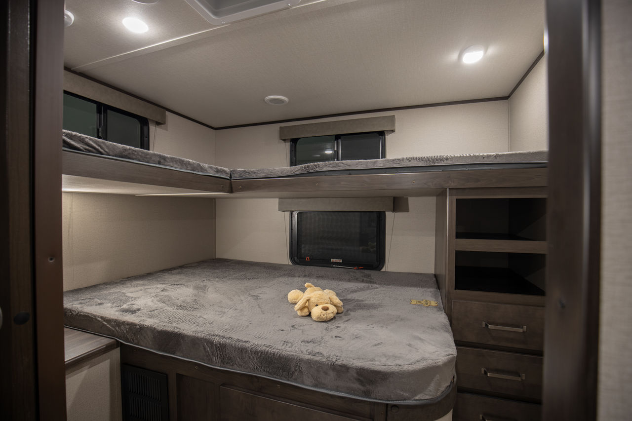 Cozy RV rental sleeping area with multi-level bunk beds, plush bedding, and a teddy bear. Includes storage.. Grand Design Transcend Xplor 2021