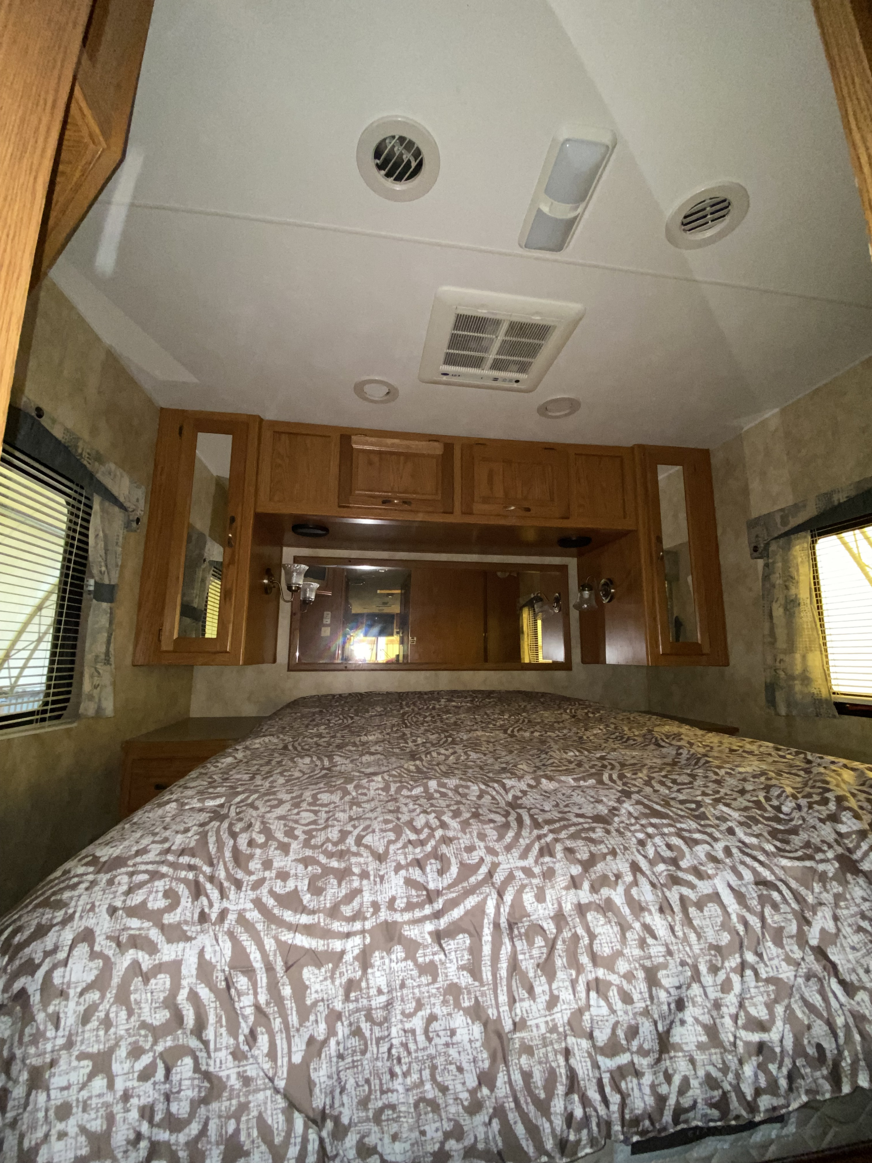 RV rental bedroom: A comfortable bed with brown and white patterns, wood cabinets, ceiling AC/lights, and reflective surfaces.. Damon Corporation Daybreak 2006