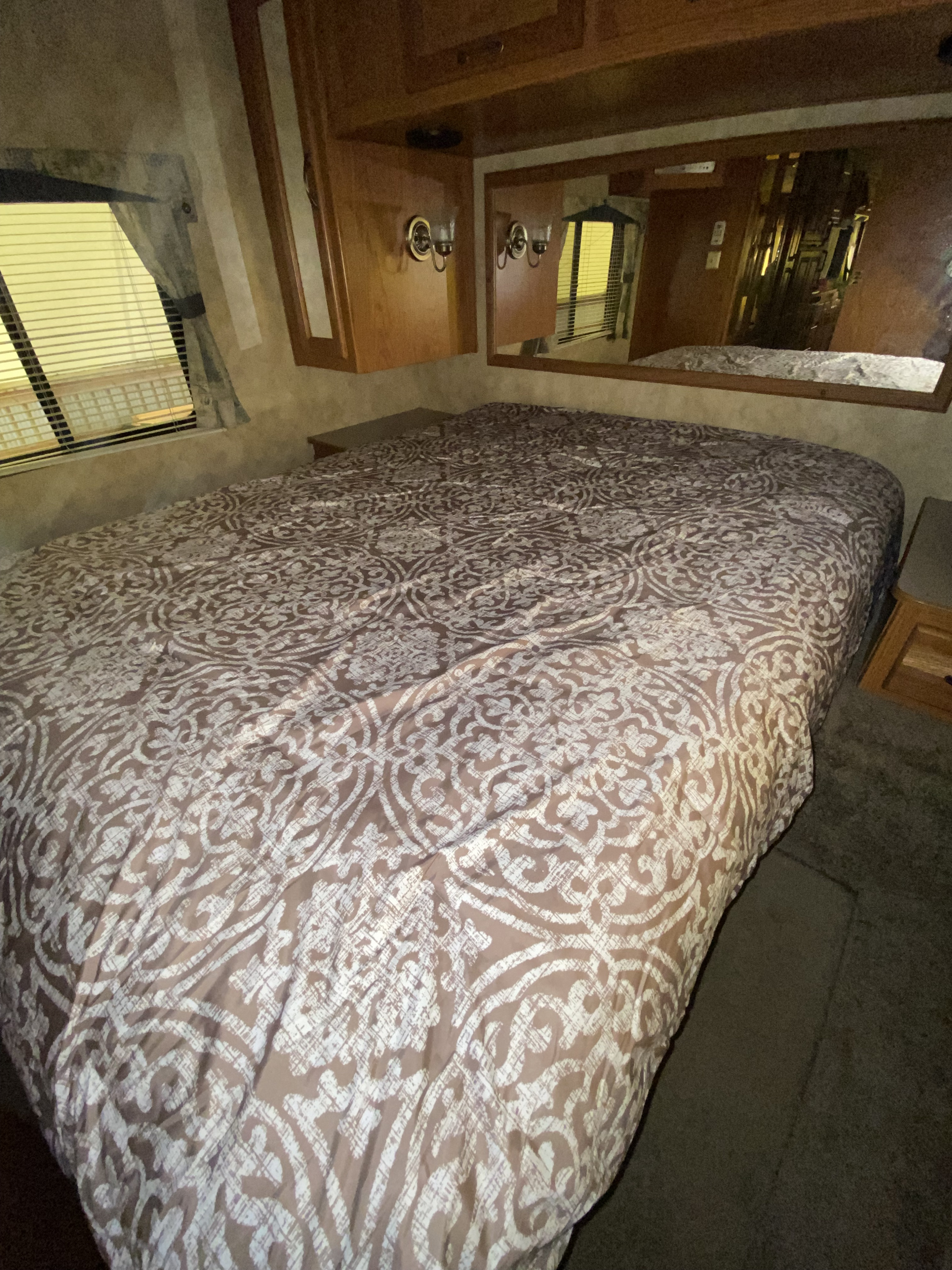 Cozy RV rental bedroom with a comfy patterned bed, window, and wood cabinetry. Perfect for your next travel adventure.. Damon Corporation Daybreak 2006