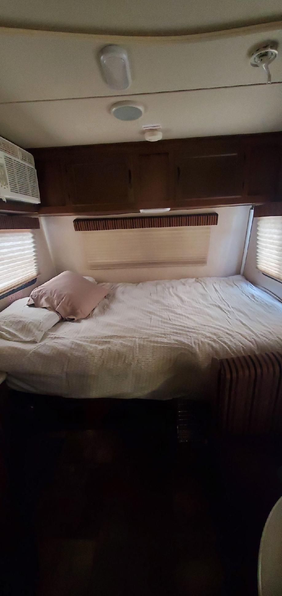 Cozy RV rental bedroom featuring a comfortable bed, dark wood overhead cabinets, window blinds, and AC unit.. Jayco Jay Flight Swift SLX 2014