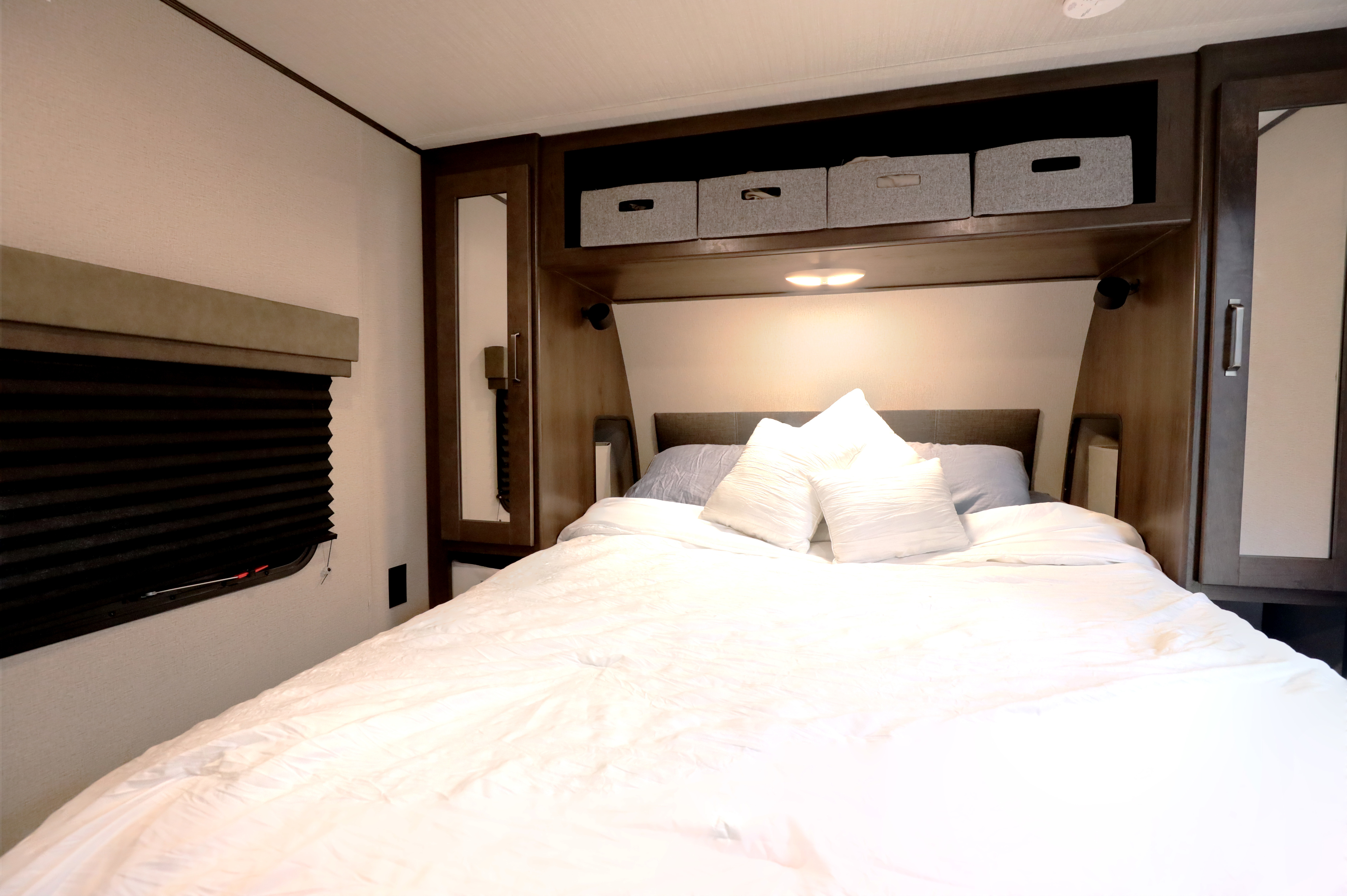 Cozy RV rental bedroom with fresh white bedding, overhead storage bins, and window blinds. Ideal for comfortable travel.. Grand Design Transcend Xplor 2022