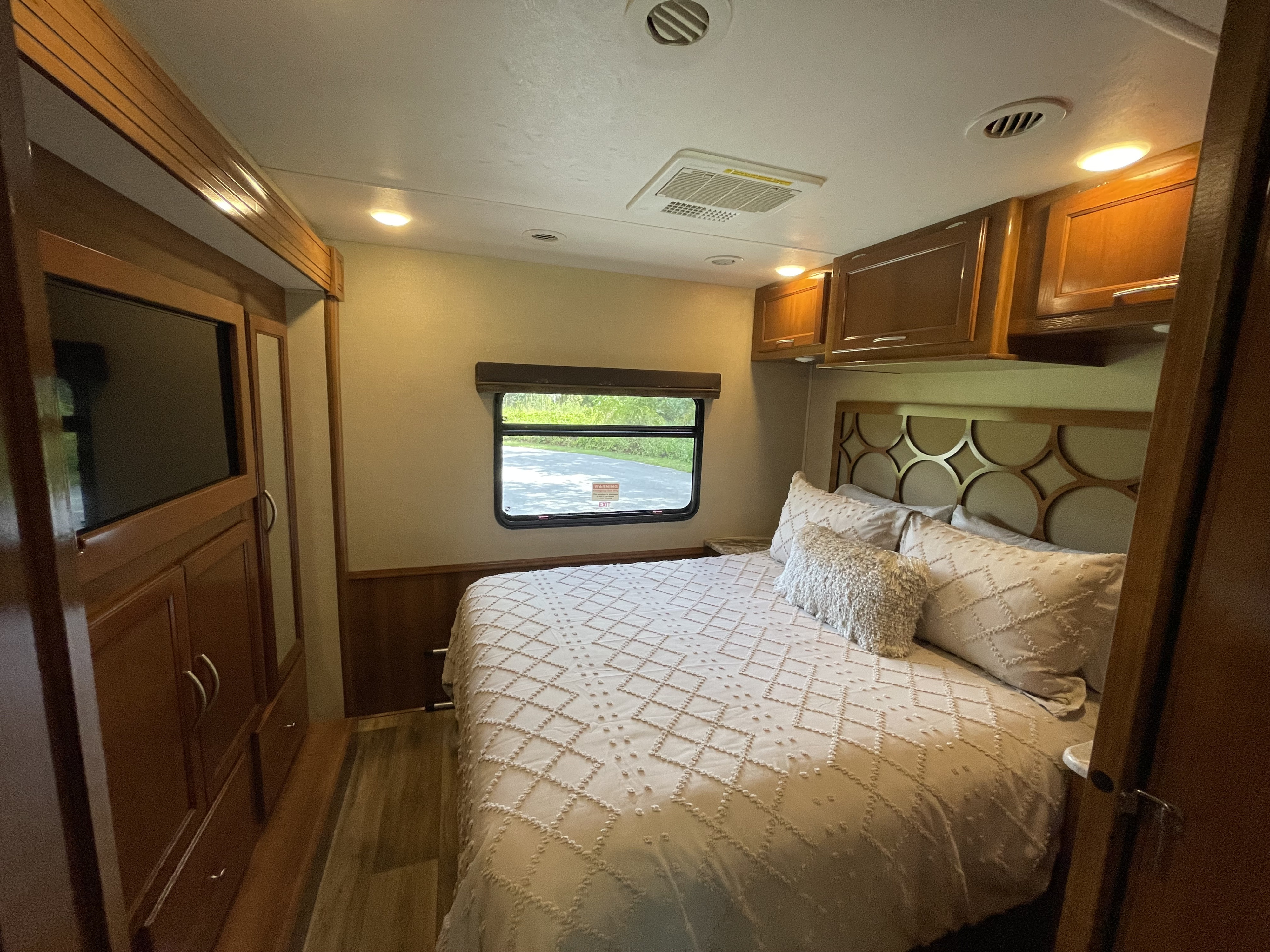 RV rental bedroom interior with a comfortable bed, decorative headboard, window, and wood cabinetry.. Coachmen Pursuit 2019