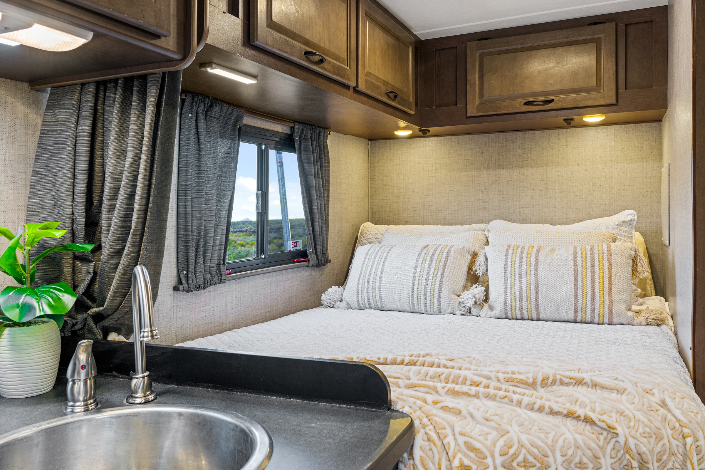 Cozy RV rental bedroom with plush bed, window, and compact sink area.. Thor Majestic 2019