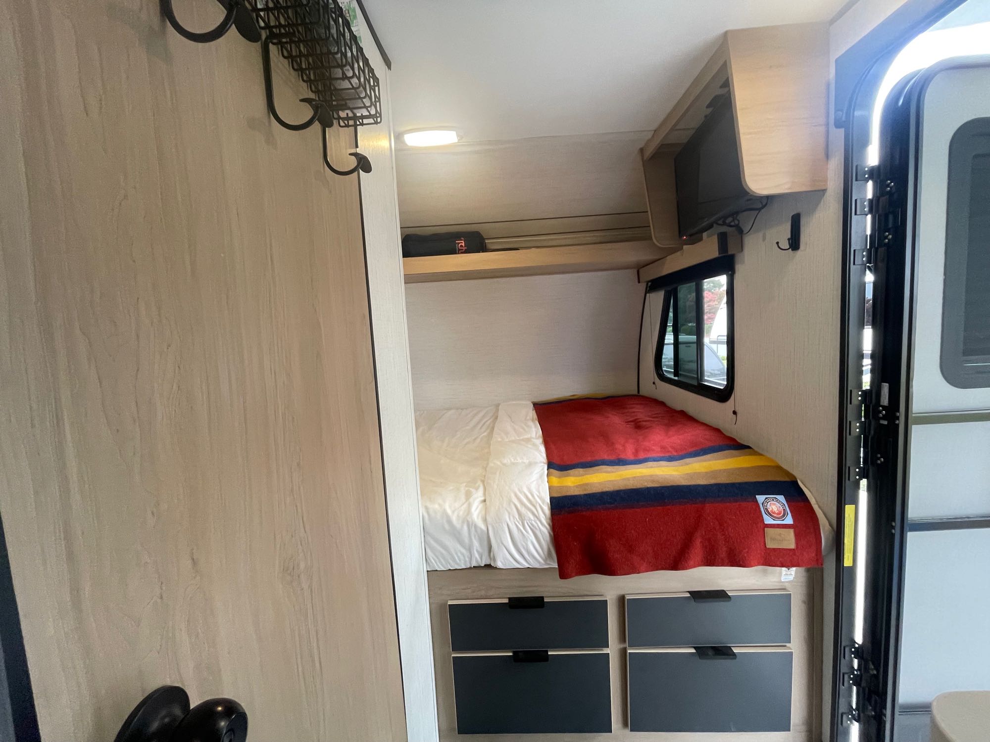 Inside a compact RV rental: a cozy bed with colorful blanket, mounted TV, and built-in storage.. Cruiser RV Hitch 16RD 2022