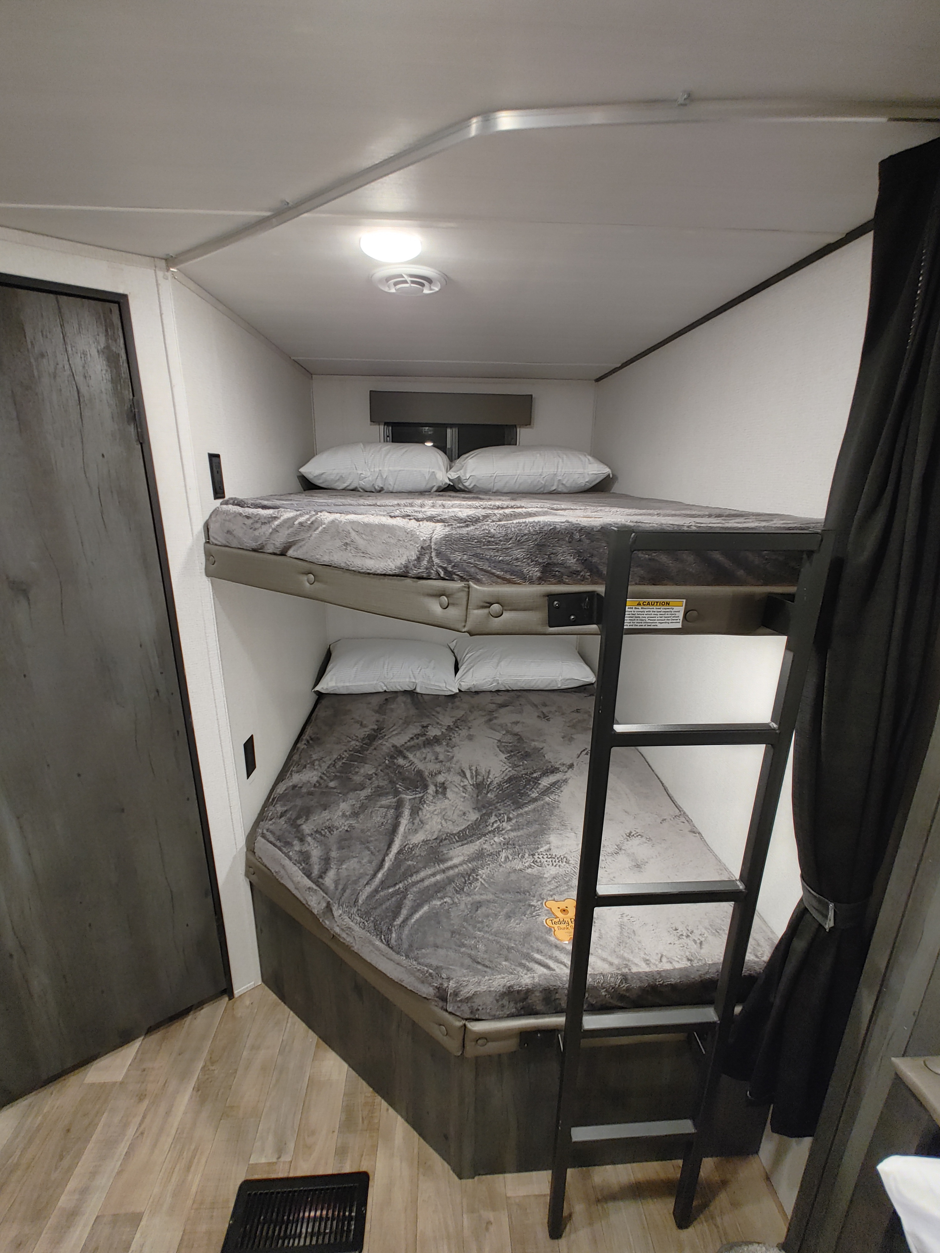 Inside an RV rental, this bunk bed setup offers two cozy sleeping areas with grey bedding and a ladder.. Keystone RV Hideout 2023